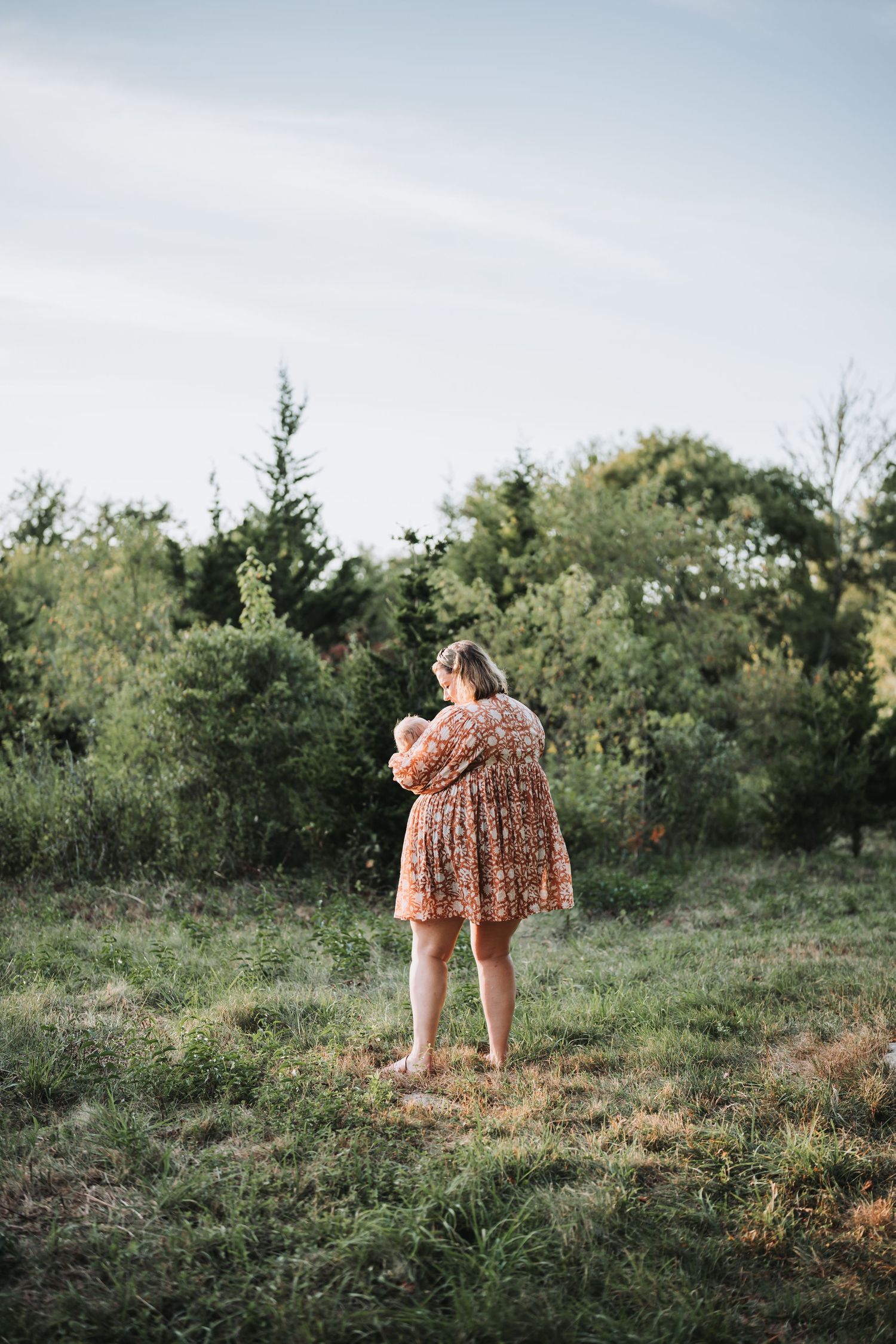 People walking on grassy hill at sunset wearing flowy dresses.