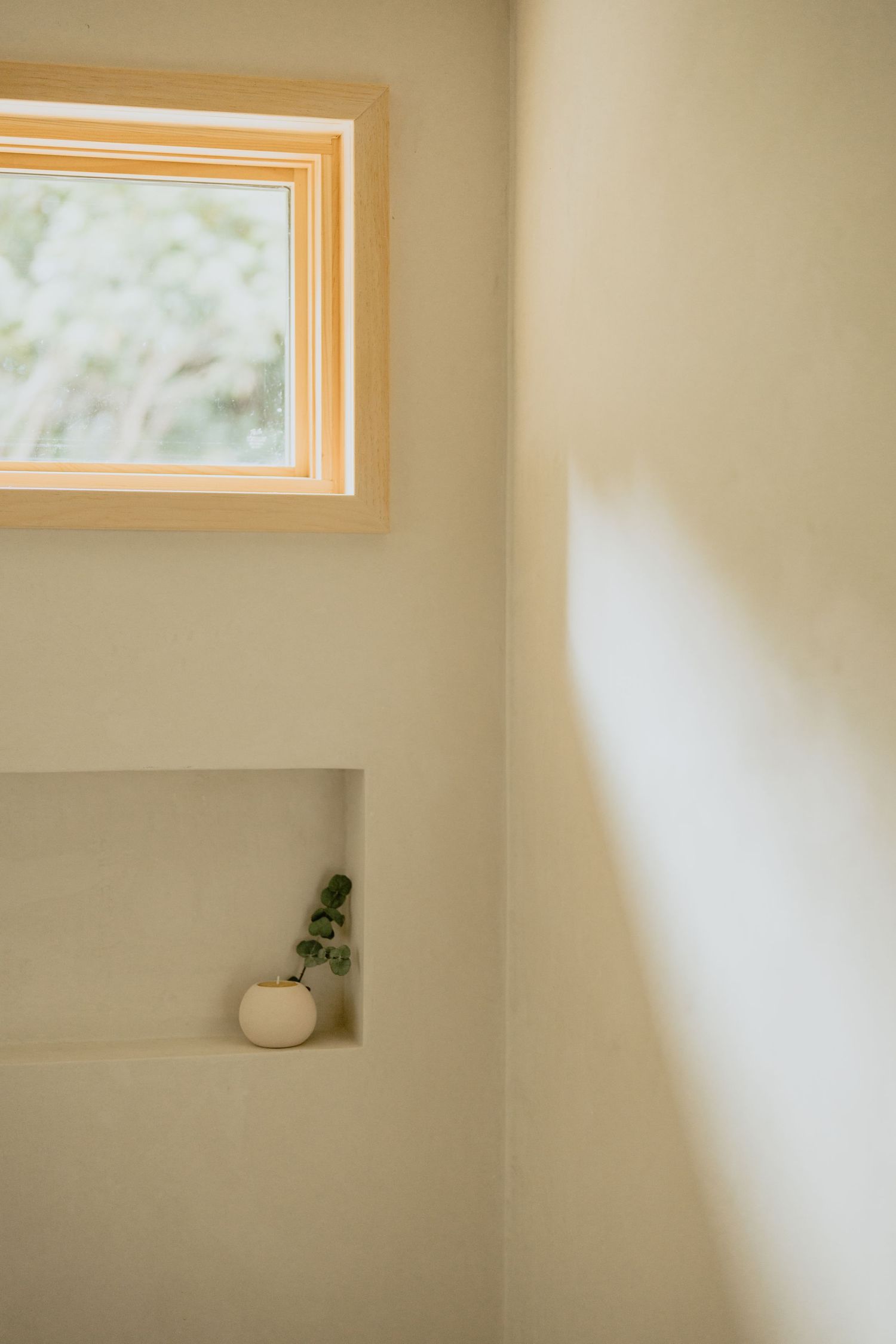 Simple white wall with window and built-in shelf holding decorative items.