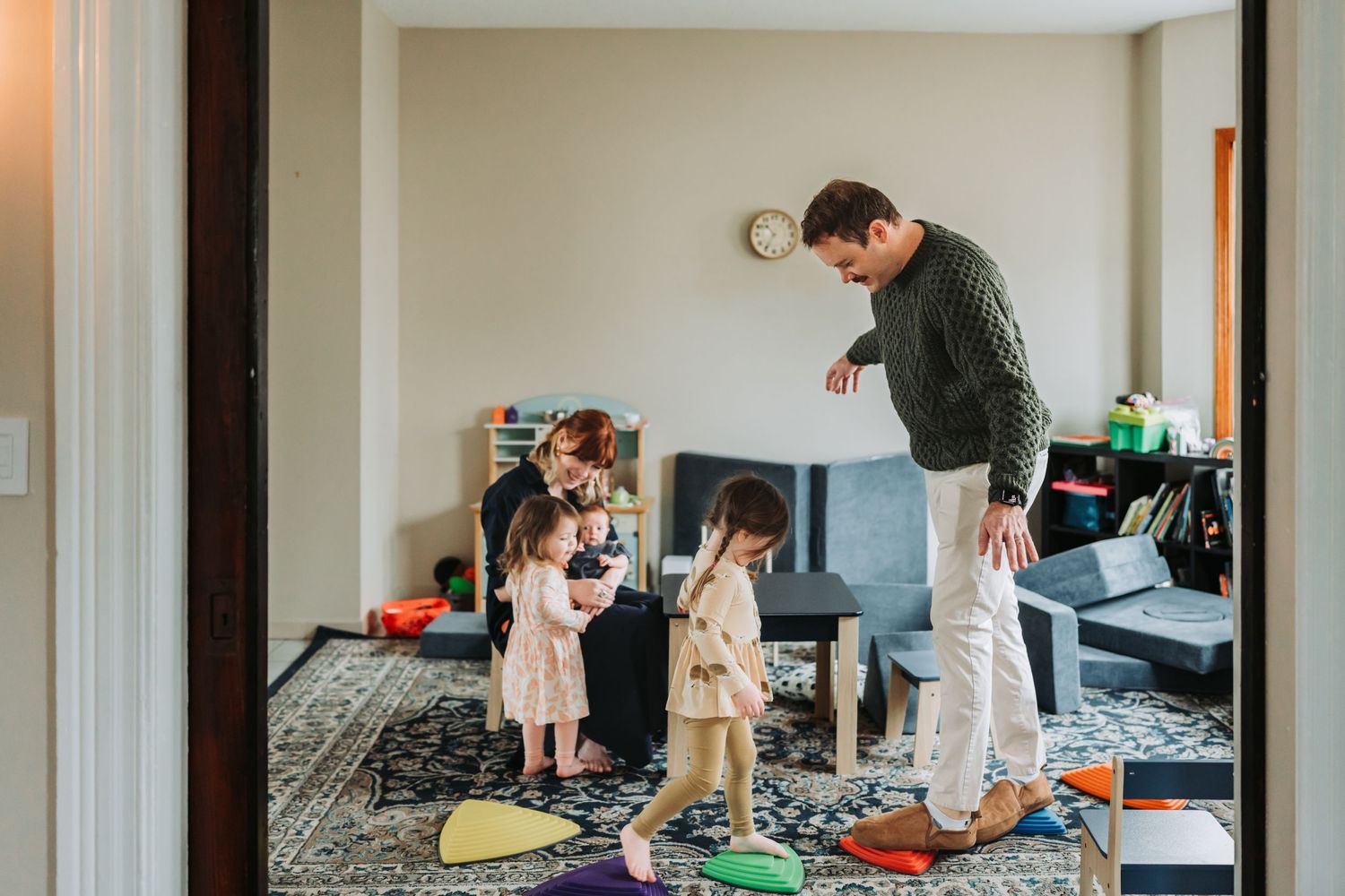 Parent and children playing with toys scattered across a living room floor.
