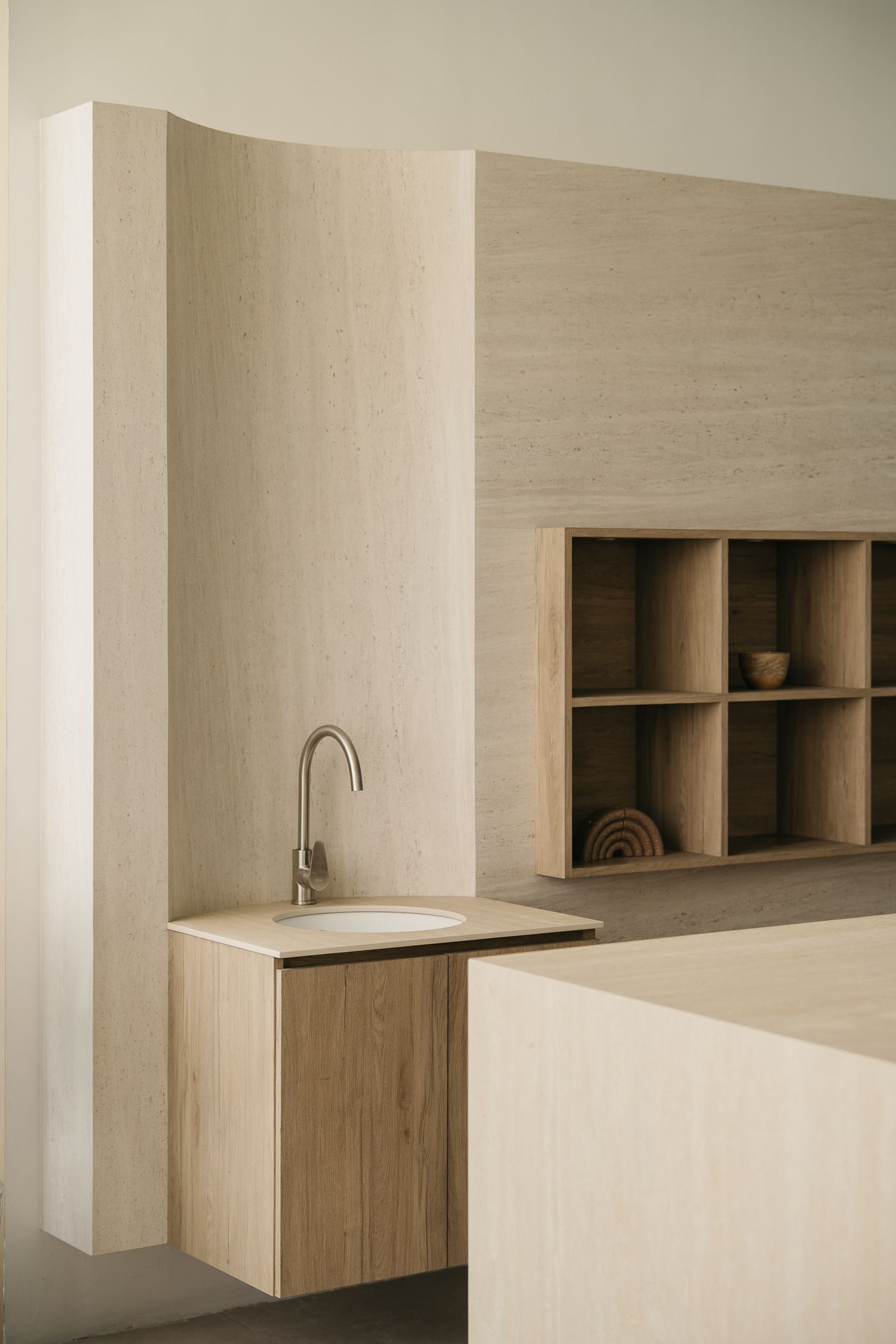 Minimalist beige kitchen interior with built-in wooden cabinets and sleek floating shelves against a neutral wall.