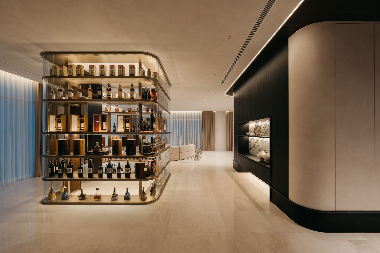 Modern interior bar with illuminated shelves displaying bottles of liquor against a sleek white wall.