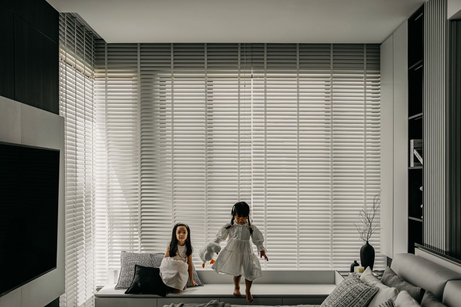 Modern living space with large windows, horizontal blinds, and minimalist decor in monochromatic tones.