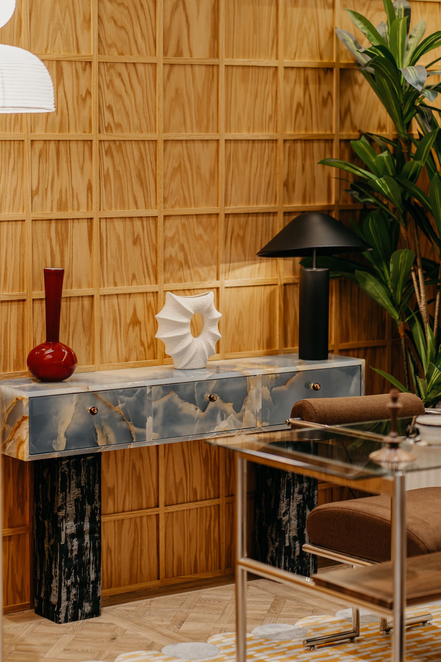 Contemporary console table with marble accents and decorative objects against wooden paneled wall.