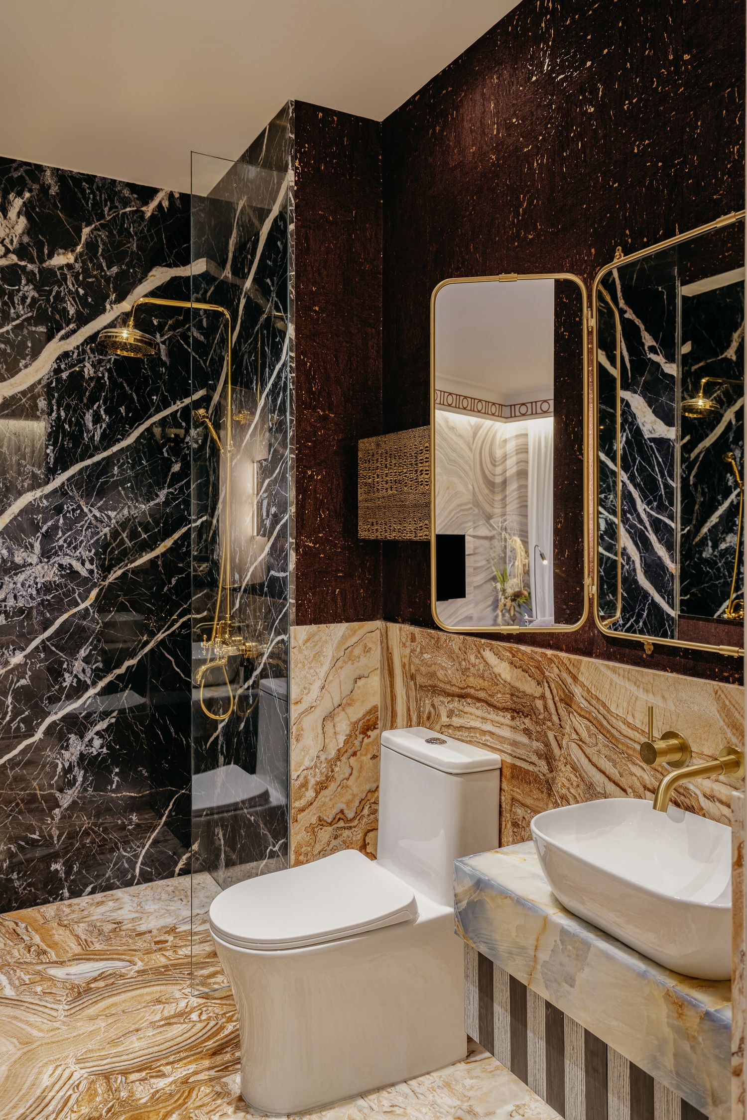 Contemporary bathroom featuring black marble walls and gold fixtures with vessel sink.