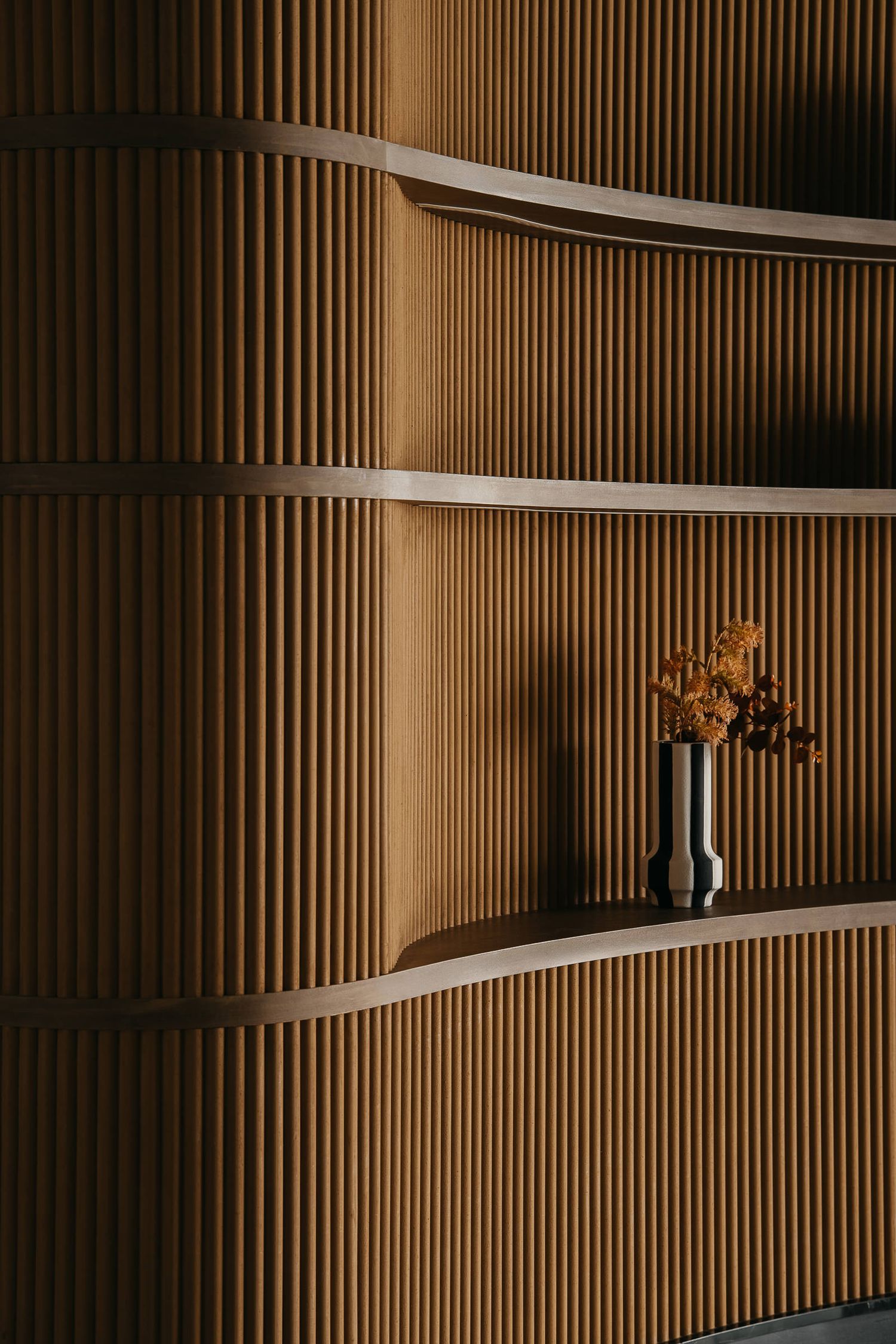 Modern architectural interior with wooden slat wall paneling and curved white shelving creating elegant minimalist design.