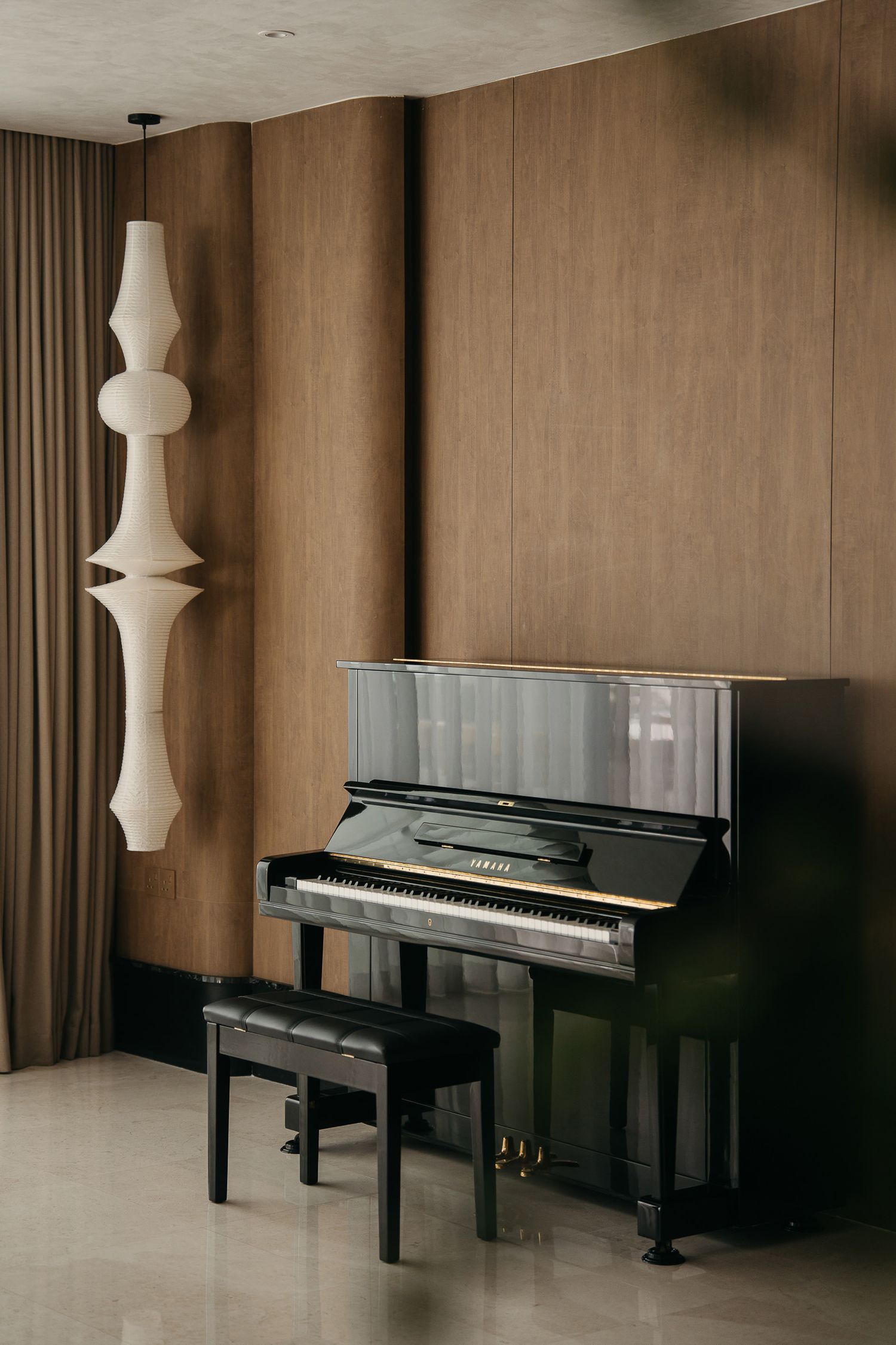 Black grand piano in minimalist room with beige walls and white pendant light creates elegant atmosphere.