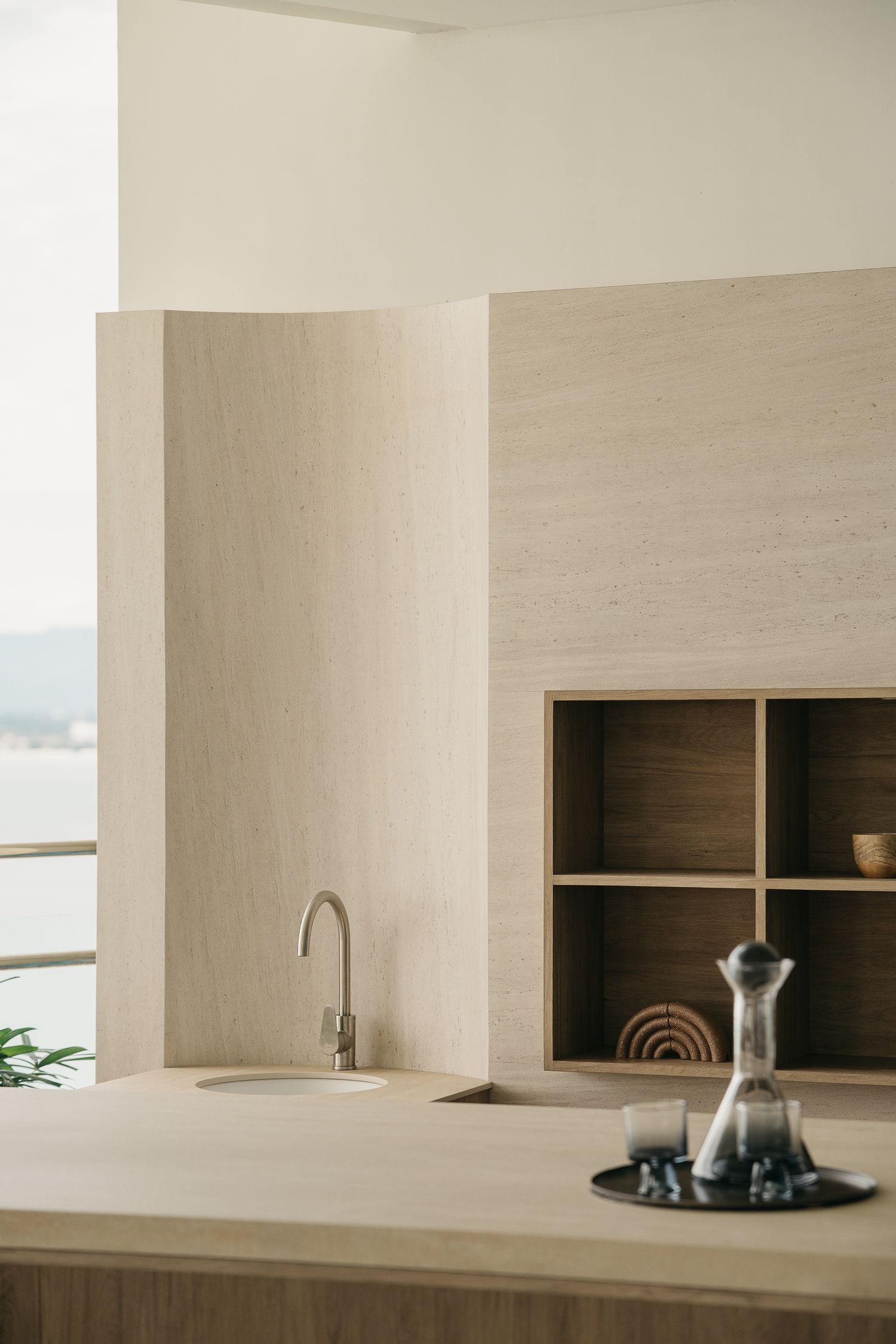 A minimalist beige kitchen interior with built-in shelving and sleek countertops showcases modern architectural design.