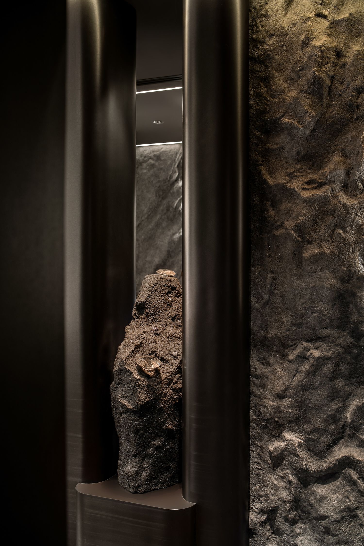 Dark stone walls with vertical metal beams create a dramatic architectural contrast in a dimly lit space.