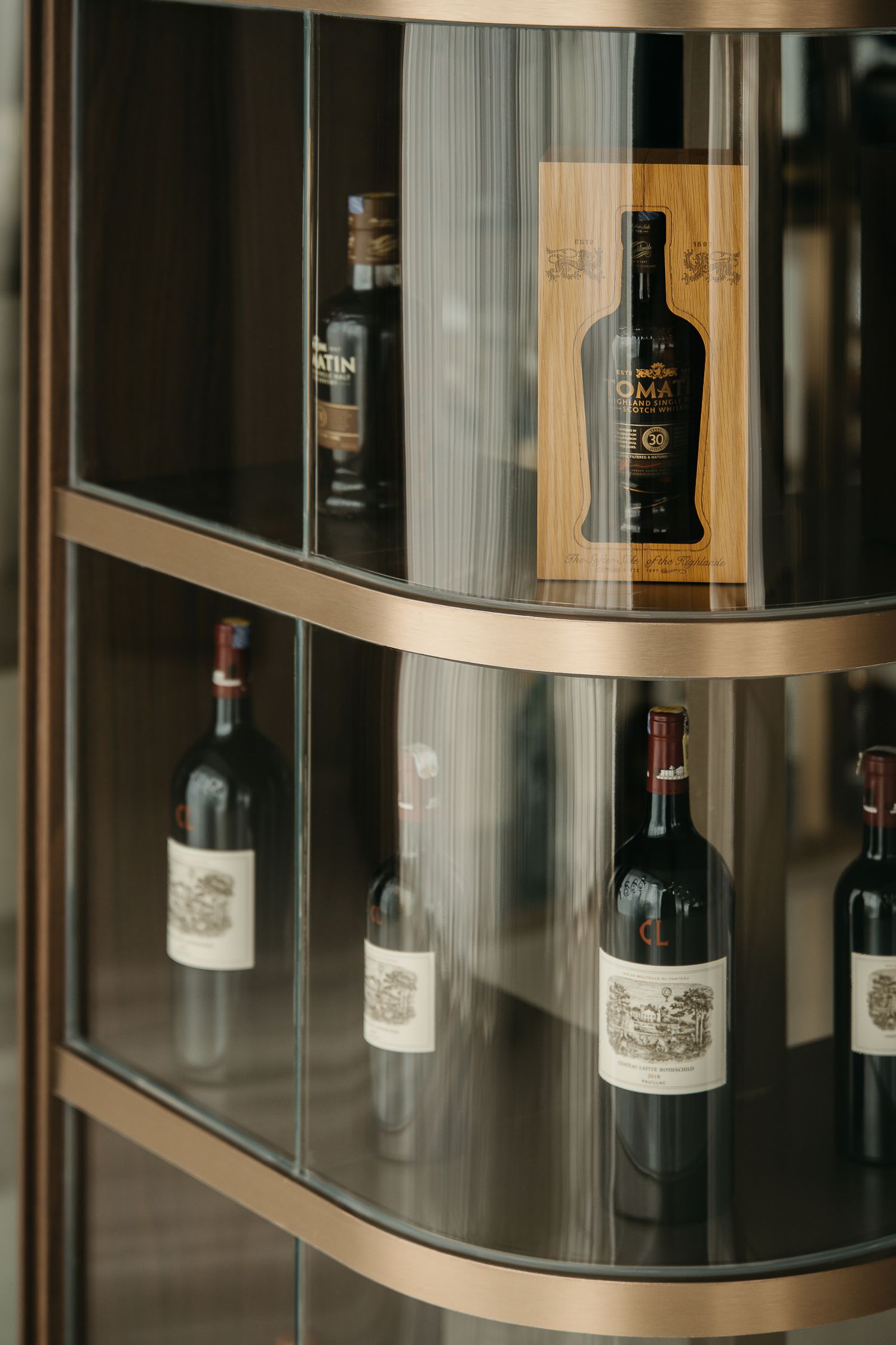 Curved wooden shelves display a collection of wine bottles in elegant glass cases with soft lighting.