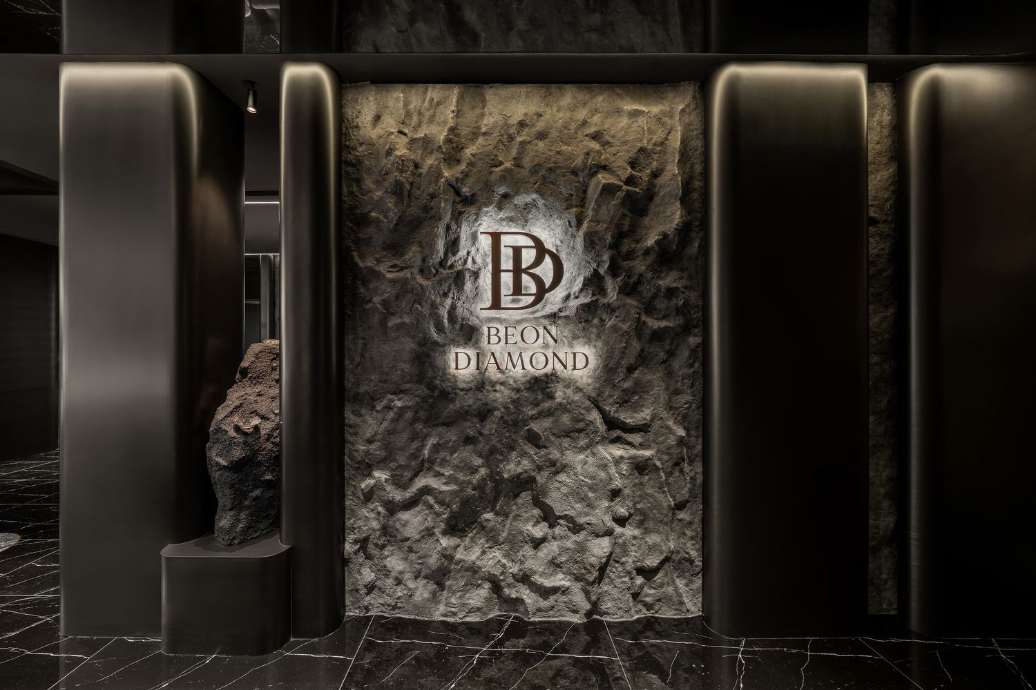 A modern luxury hotel hallway with stone walls, dark accents, and elegant lighting creates an upscale atmosphere.