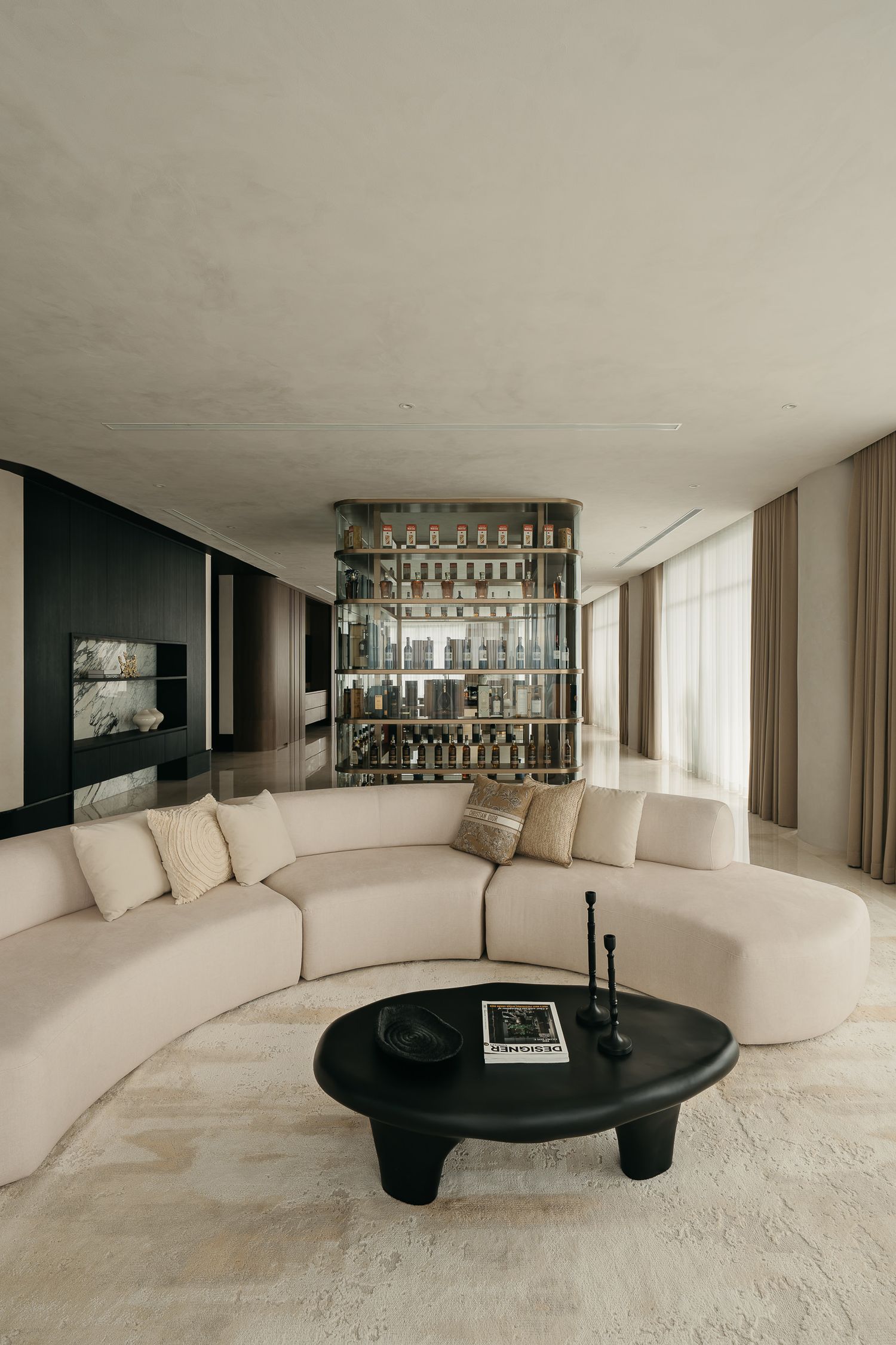 A modern curved sofa in white wraps around a black oval coffee table in a minimalist living room with art on the walls.