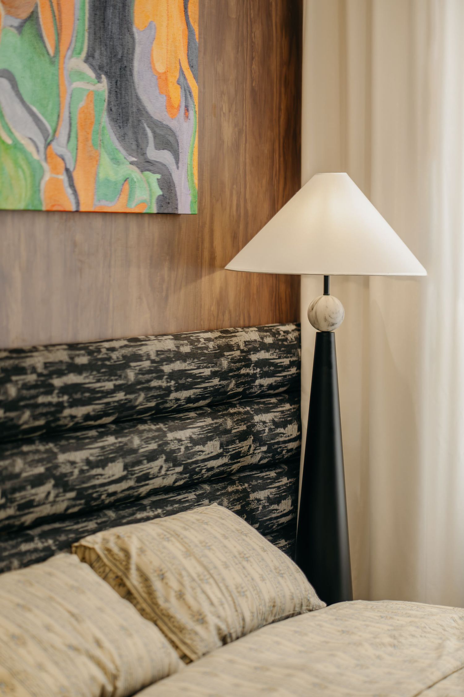 Sleek bedside lamp with conical shade next to modern abstract wall art.