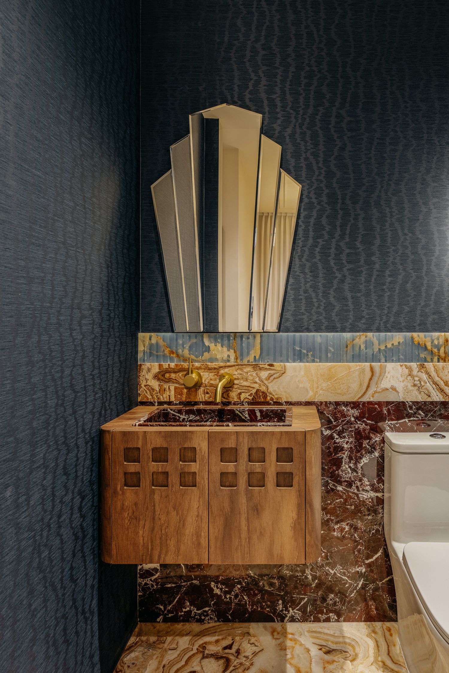 Art deco mirror with gold fan design mounted on dark textured wall above wooden cabinet.