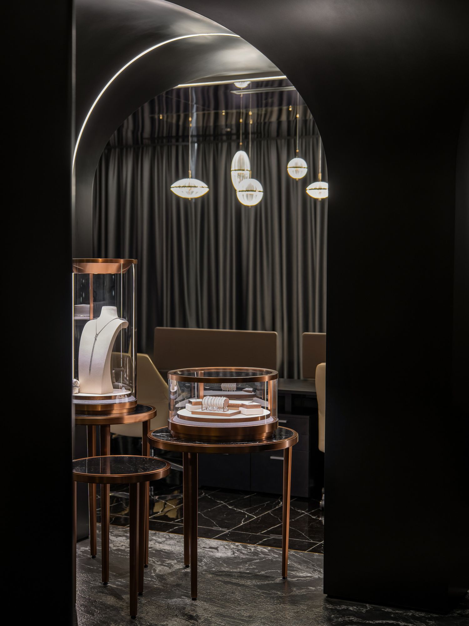 Elegant dark exhibition space featuring circular wooden display tables illuminated by pendant lights against black curtains.