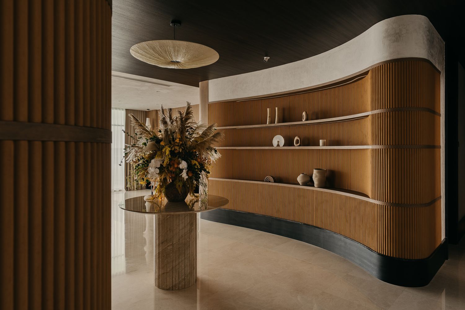 Modern curved wooden wall with built-in shelving and decorative floral arrangement in a luxury interior space.