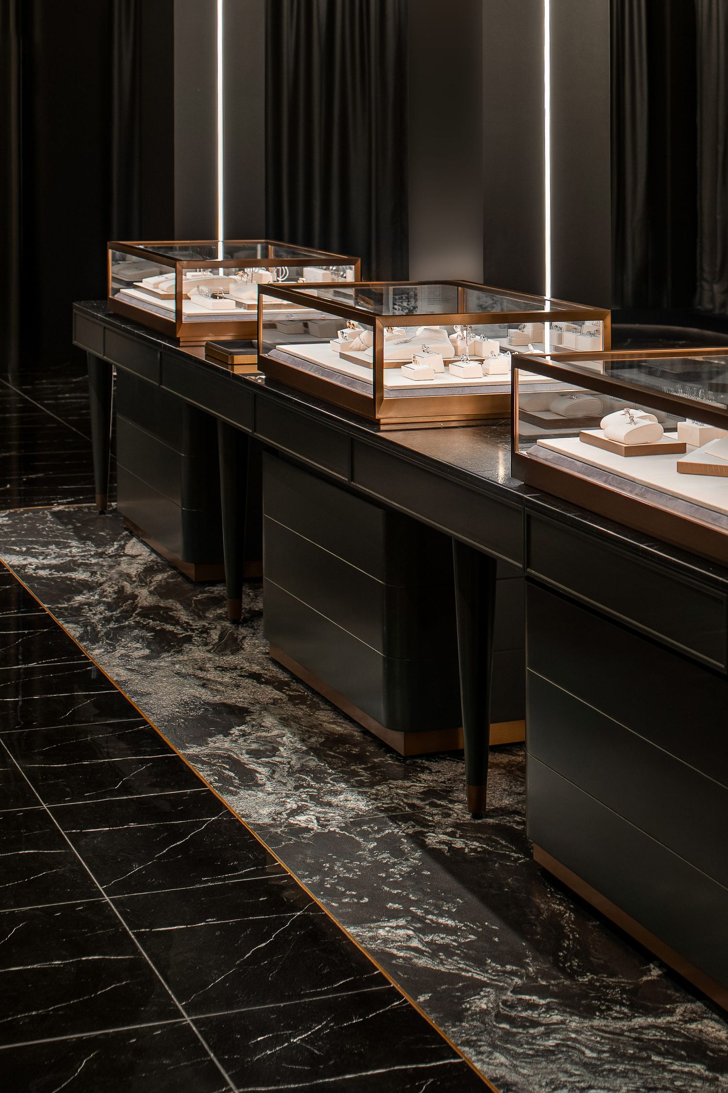 Luxury jewelry display cases with modern lighting on dark marble counters in an upscale retail store interior.