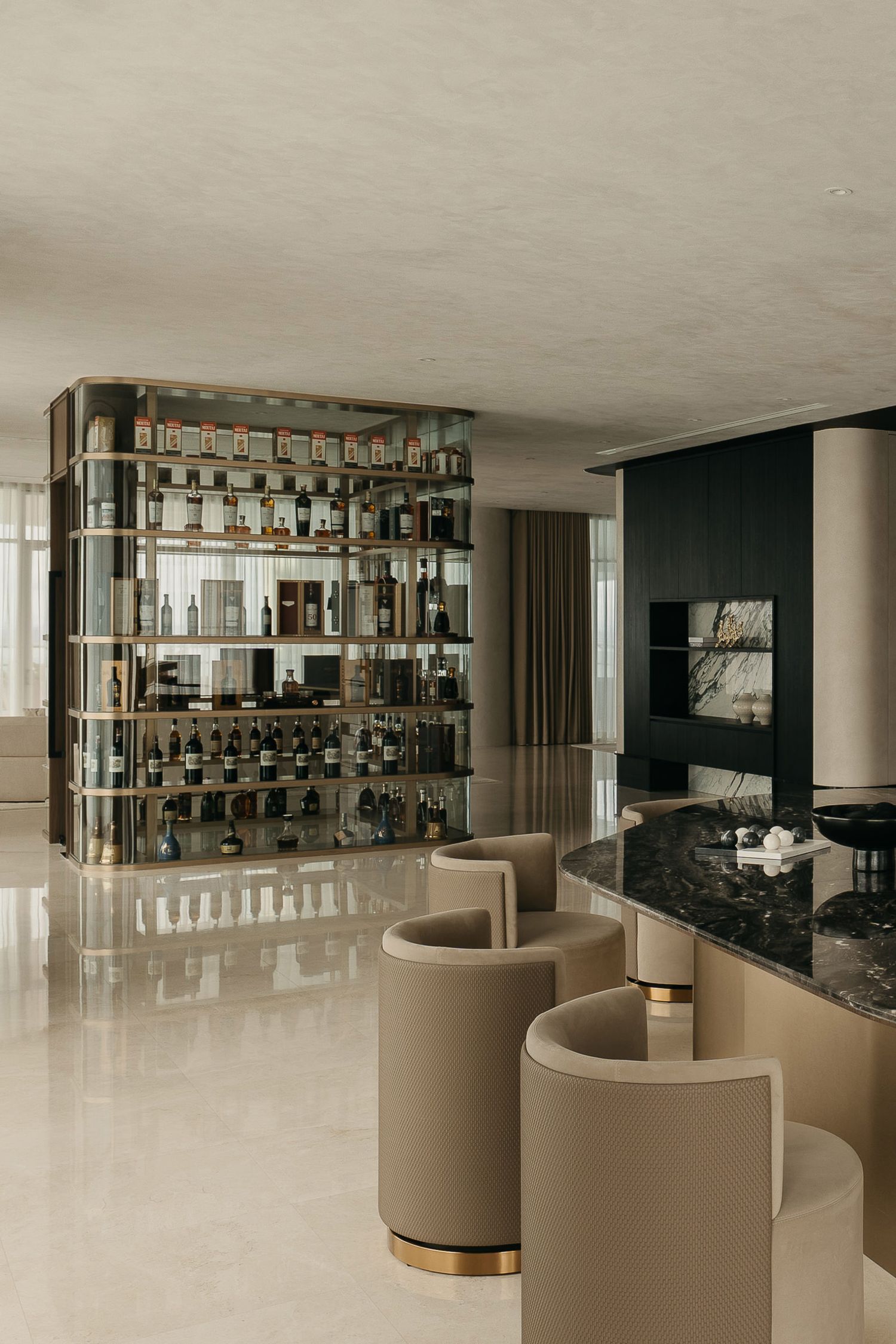 Modern luxury hotel bar interior with curved beige seating and illuminated shelving displaying bottles.