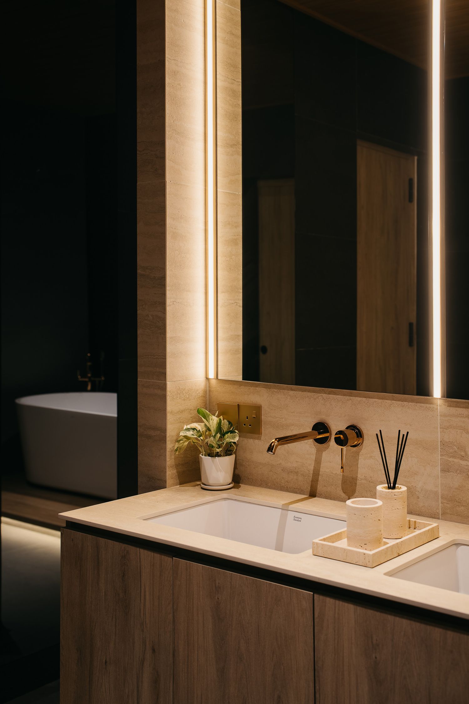 Modern bathroom vanity with illuminated mirror, wooden cabinets, and white countertop in warm lighting.