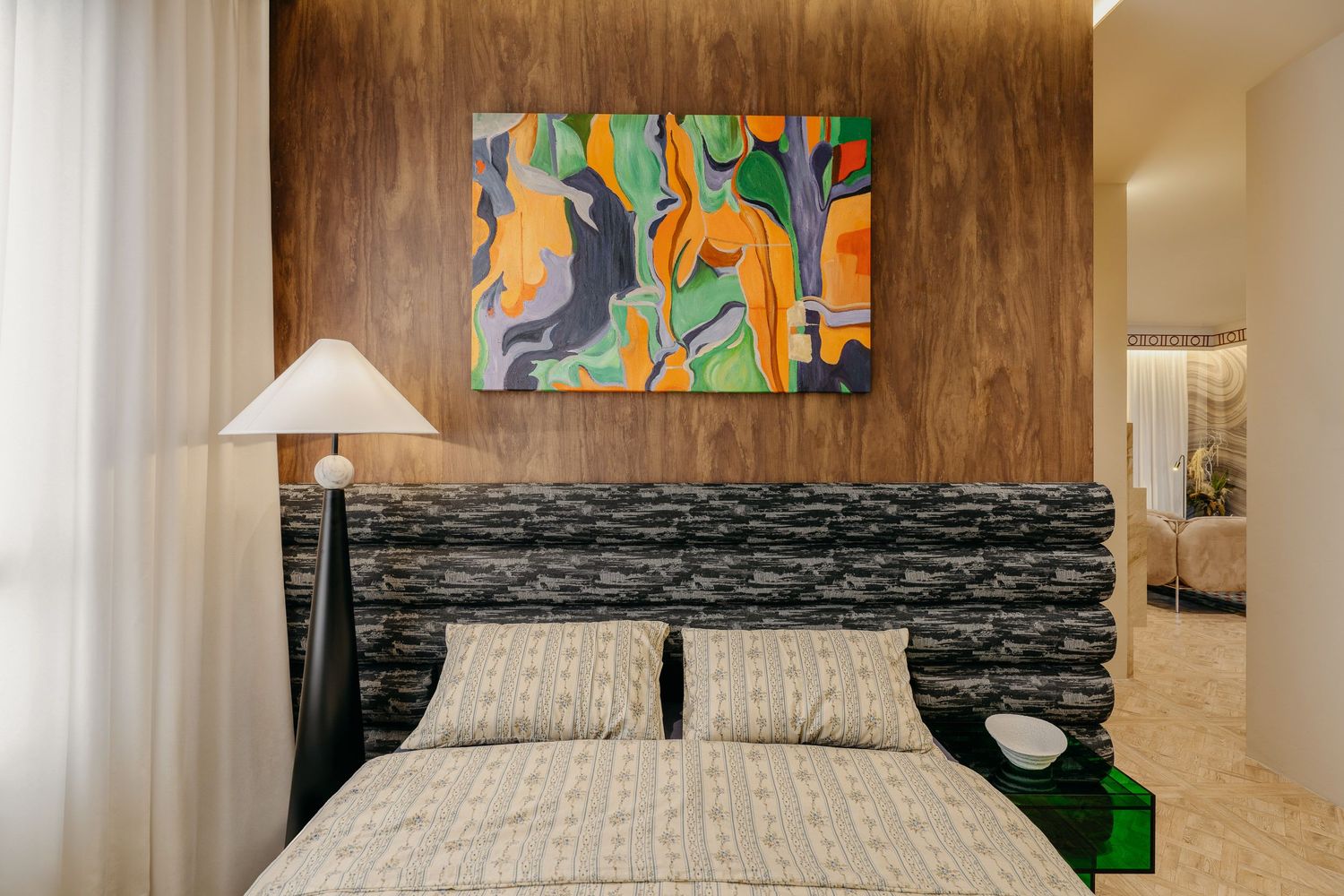 Contemporary bedroom featuring colorful abstract artwork above a dark patterned headboard.