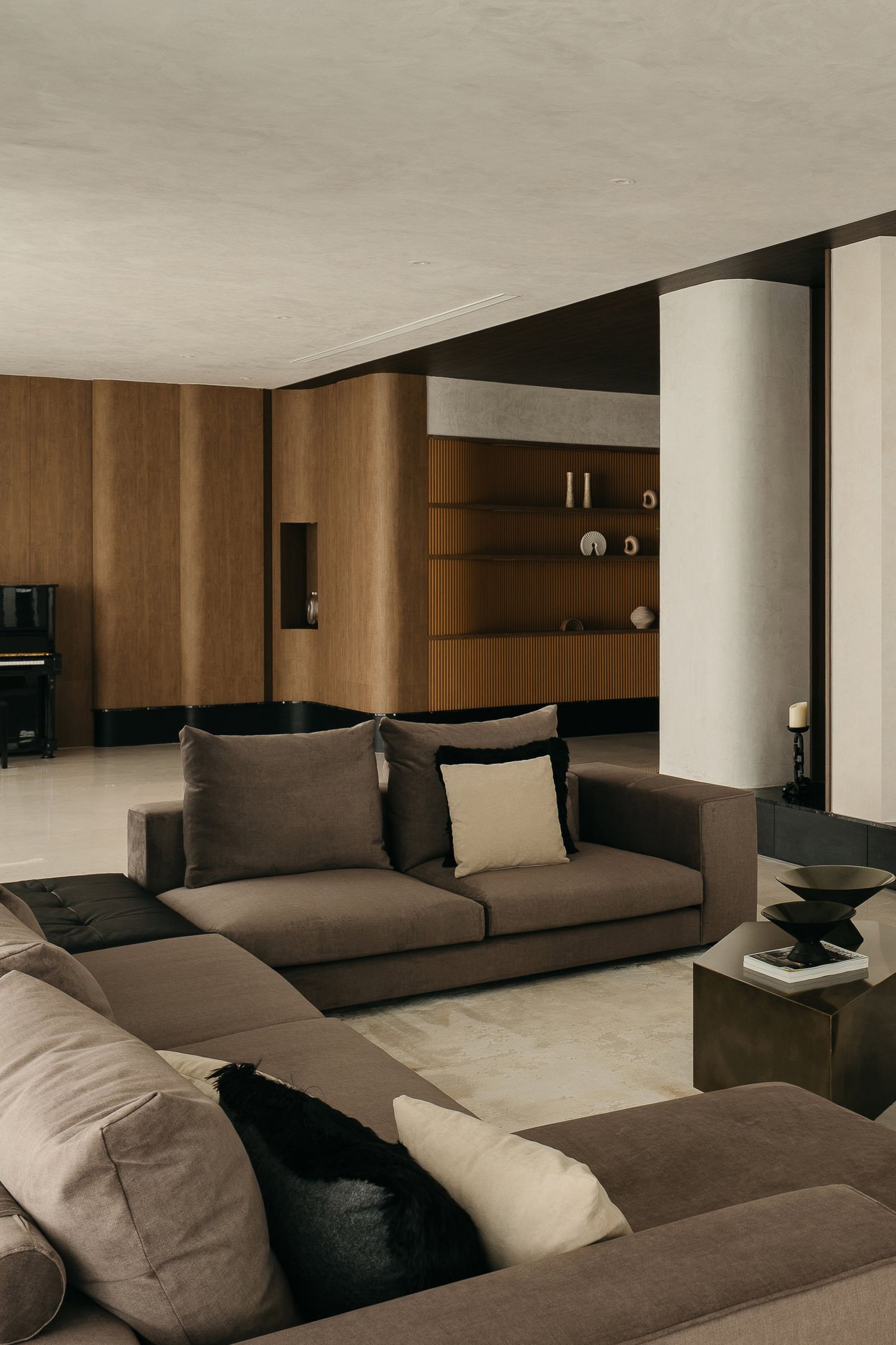 Modern living room with brown sectional sofa, wood paneled walls, and minimalist decor in neutral earth tones.