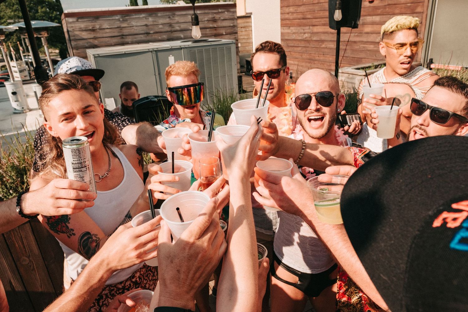 Group of friends cheering and clinking drinks together at outdoor gathering on sunny day.