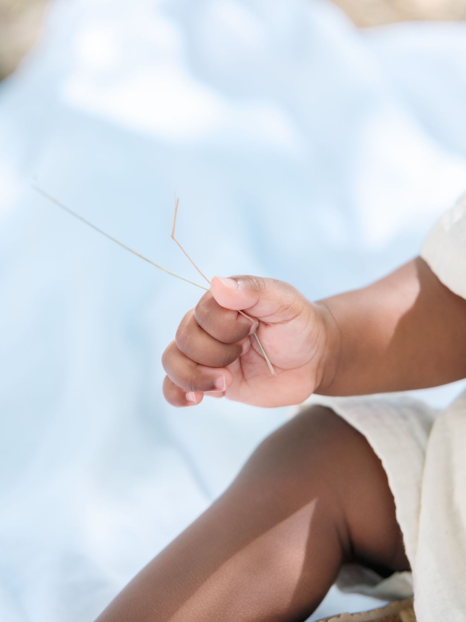 A small hand gently holds a thin hair or string against a soft blue background.