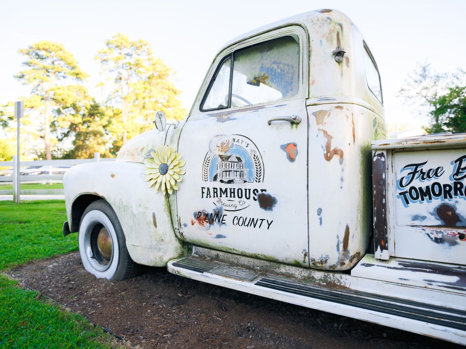 A vintage white delivery truck with farm graphics and rustic details sits parked on green grass in a rural setting.