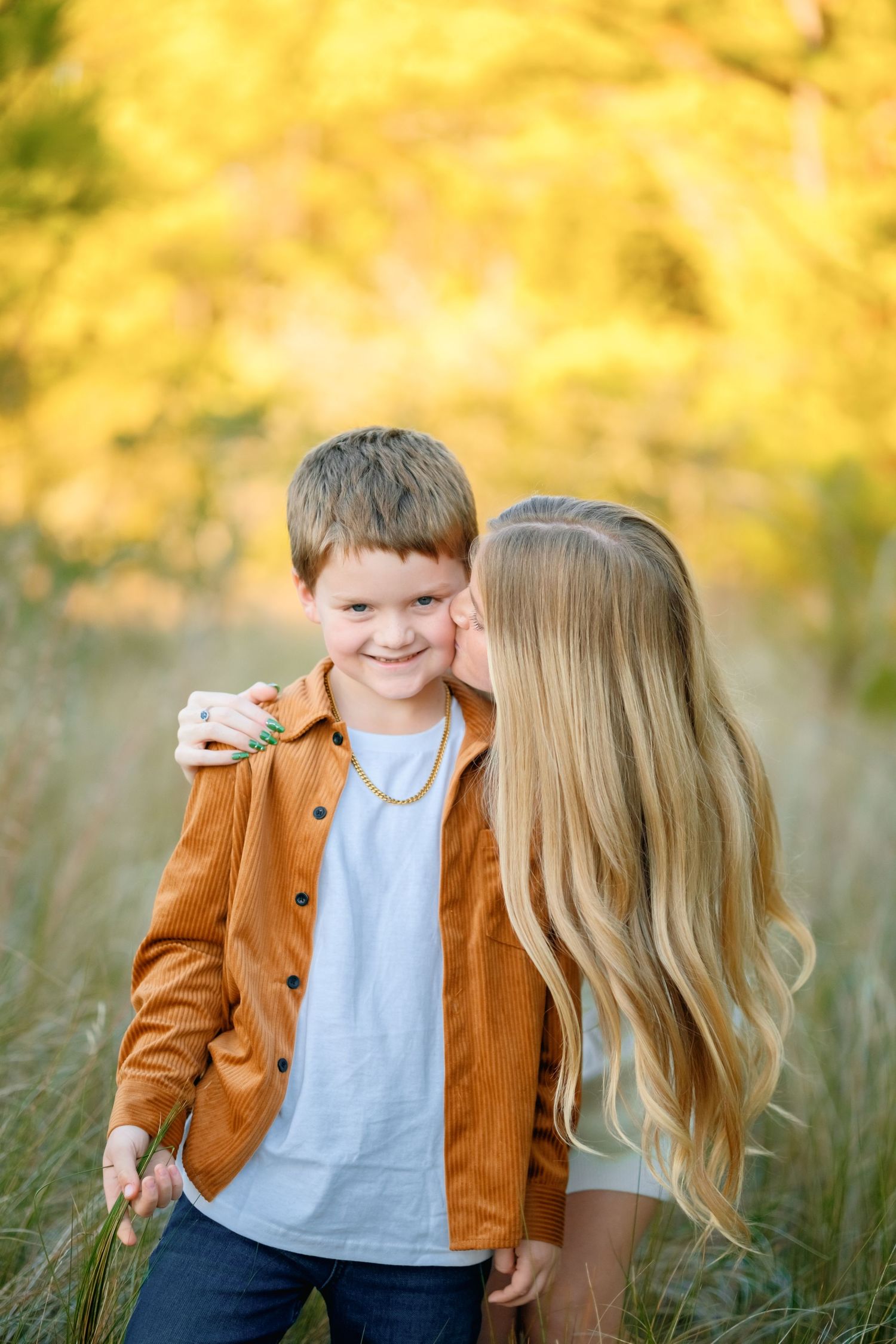 Two young children share a sweet moment together in a field with golden autumn foliage in the background.