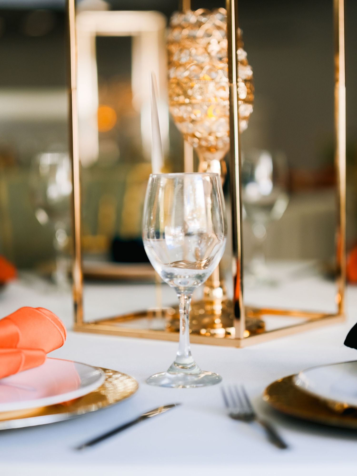 Place settings at an elegant dinner table with wine glasses, peach napkins, and gold candleholders create a luxurious ambiance.