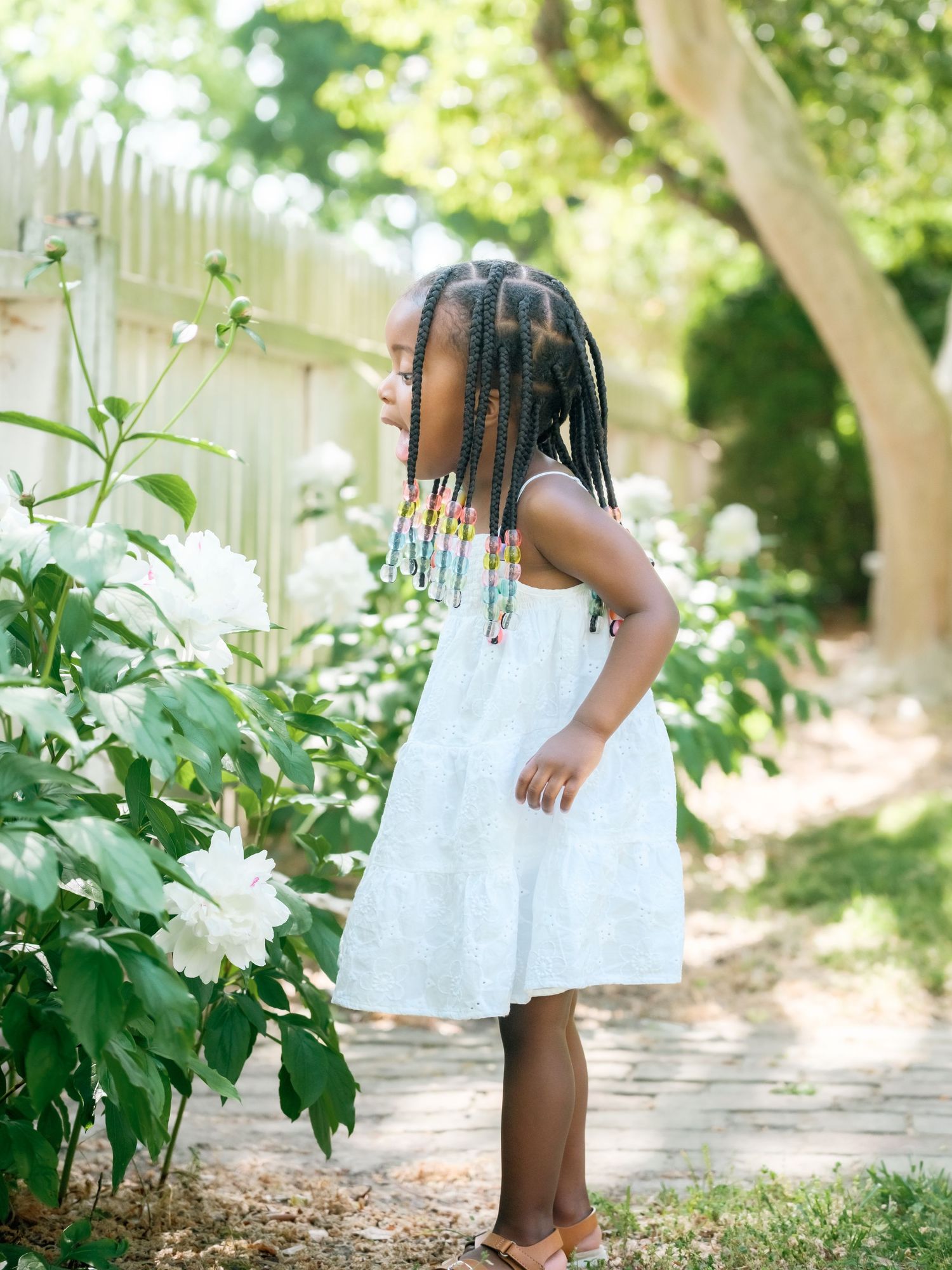 A child in a white dress walks through a lush garden path bordered by green foliage.