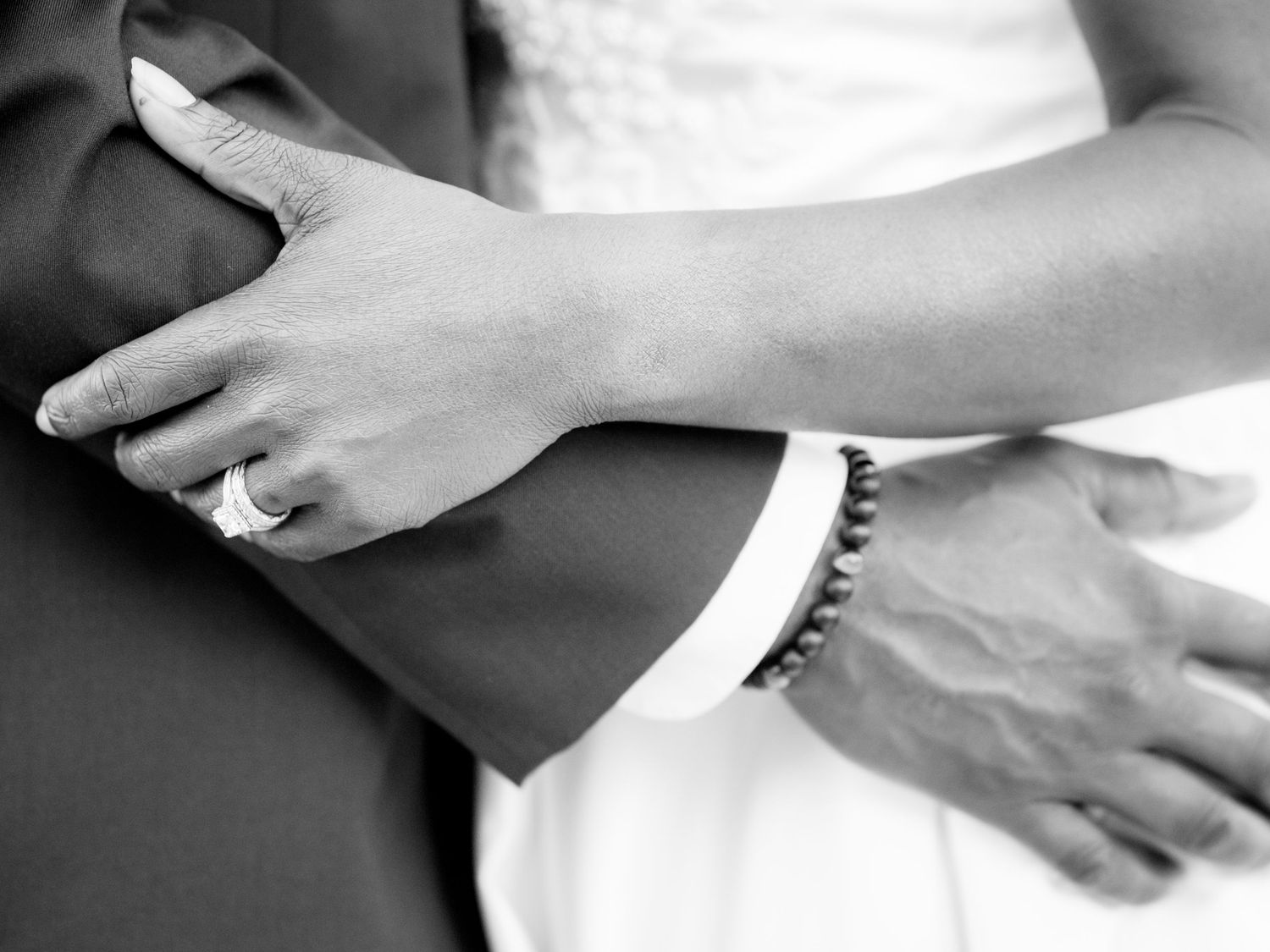 Black and white close-up of hands touching formal wedding attire.