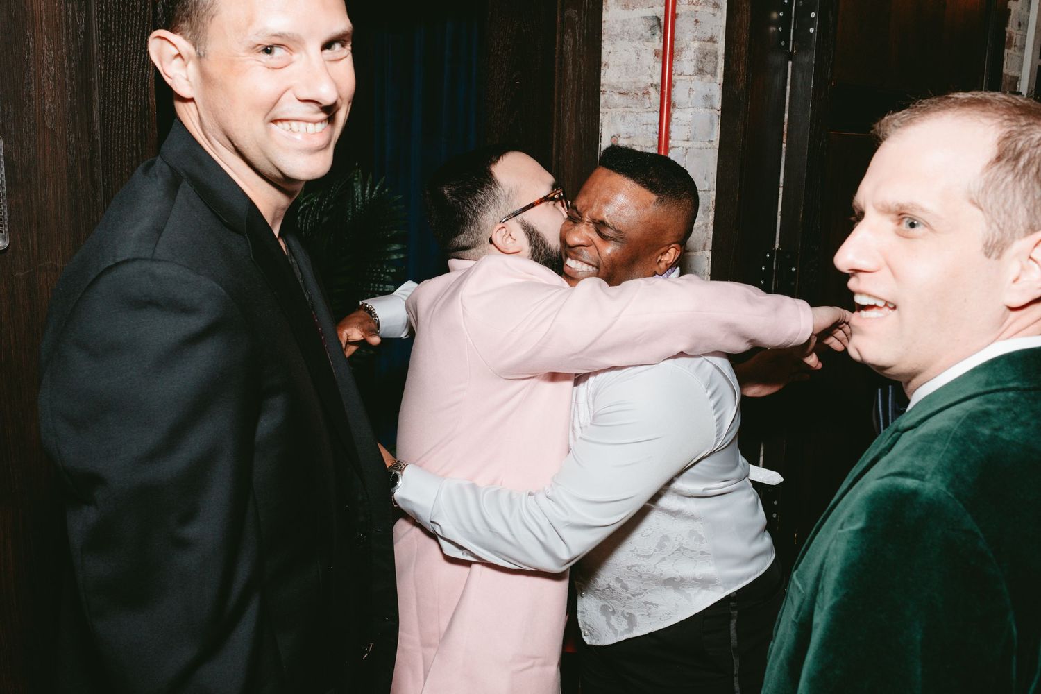 A group of friends share a candid fun moment while socializing at a dimly lit venue.
