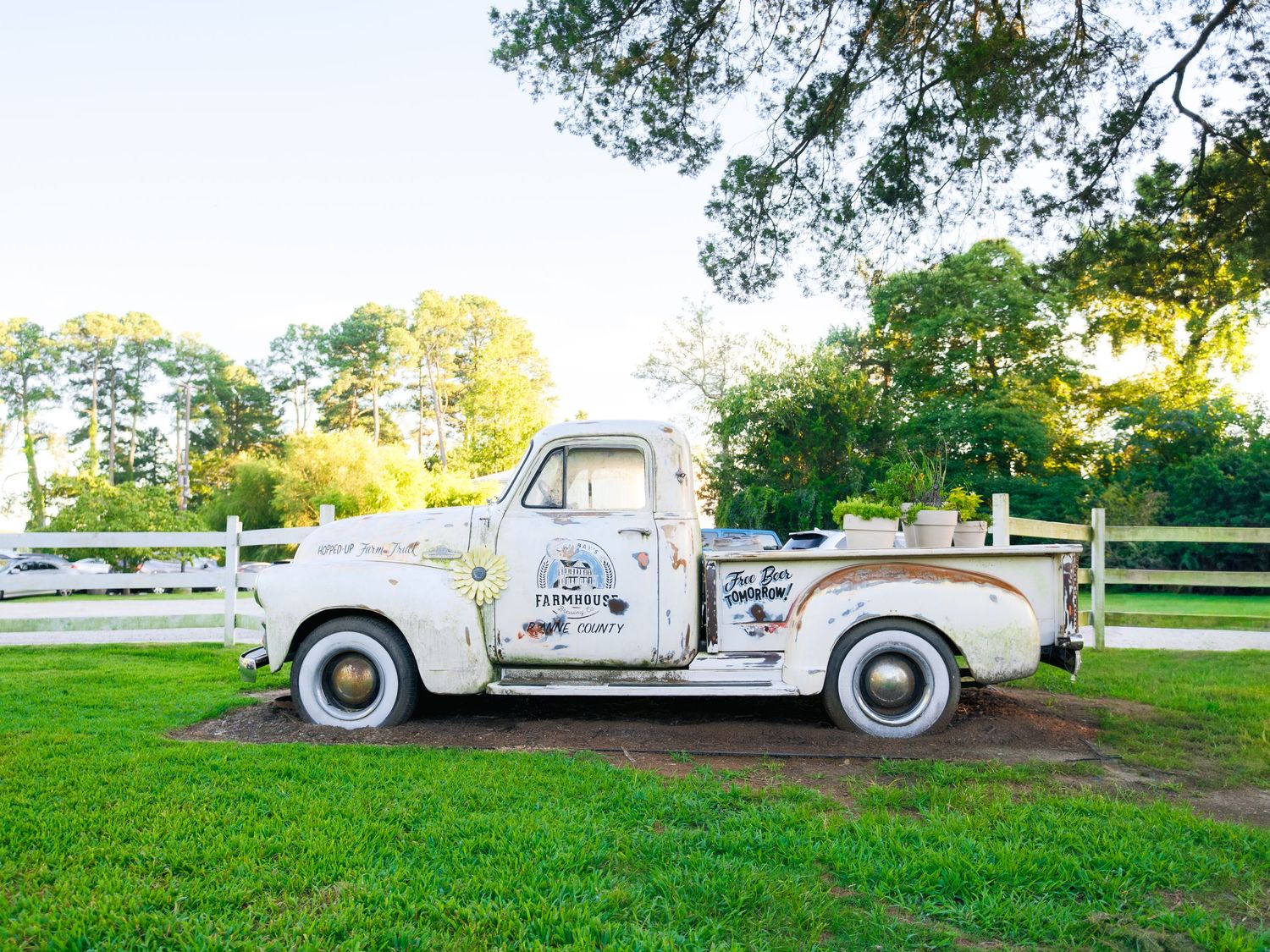 A white vintage getaway wedding car parked in a grassy field at golden hour.