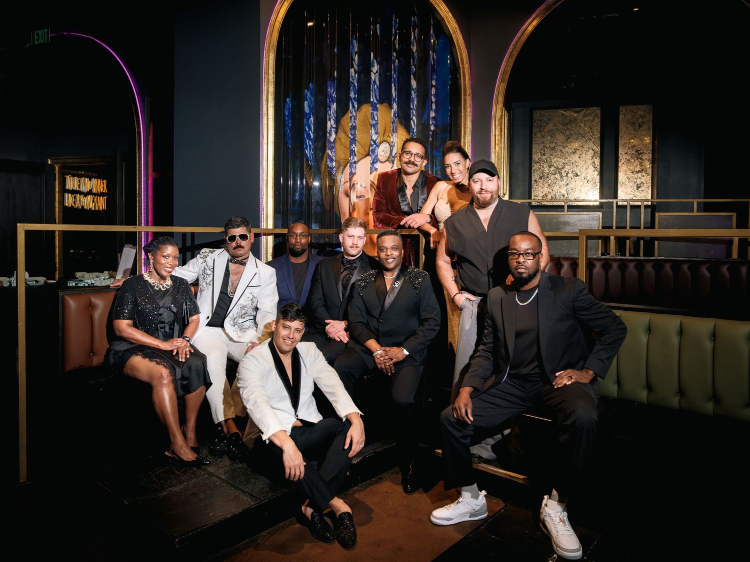 A group of people sitting on steps in a dark setting with stage lighting visible in the background.
