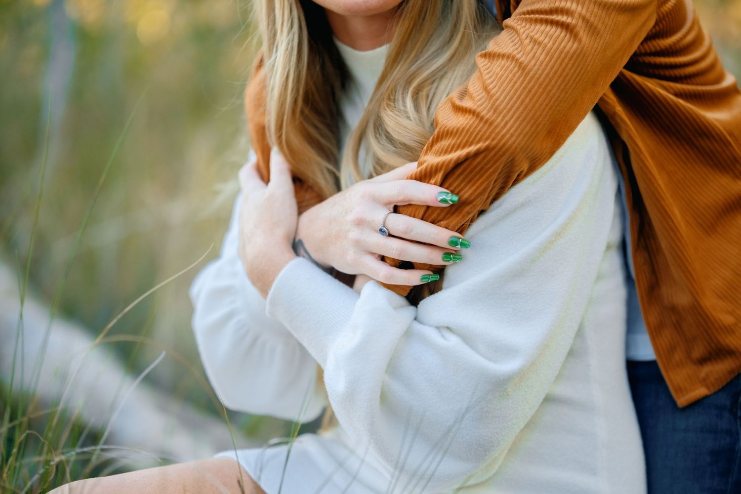 A couple embraces in a romantic outdoor setting wearing brown and white clothing against a natural background.