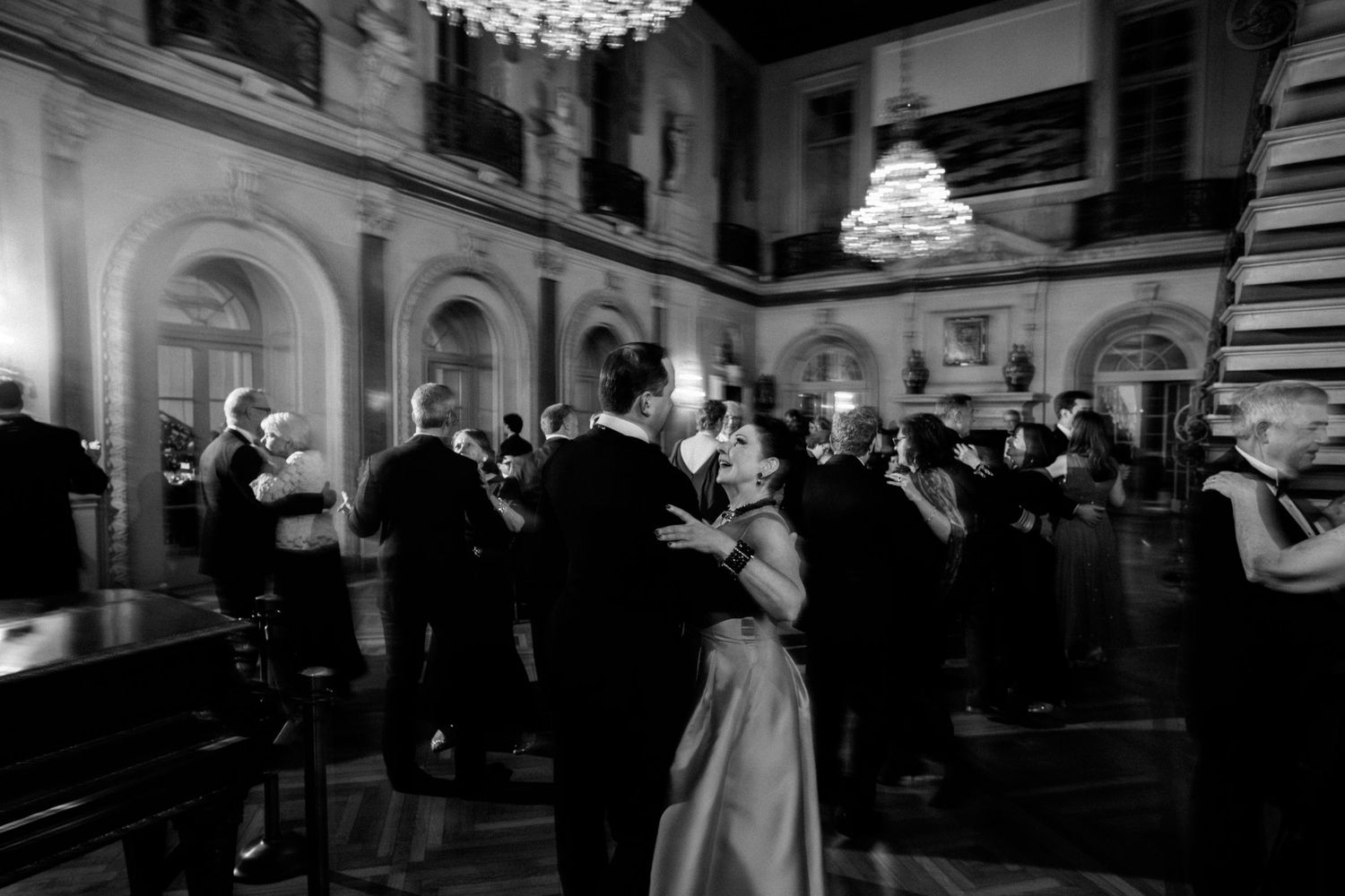 A black and white panoramic photo shows couples dancing at an elegant ballroom event with ornate architecture.