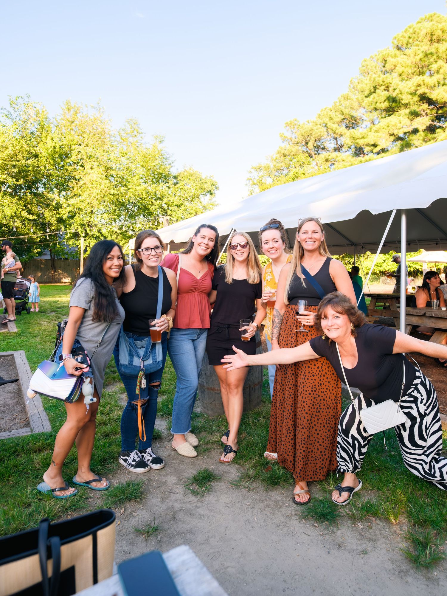 Group of friends gathered outdoors at a park celebrating together under a white tent on a sunny day.