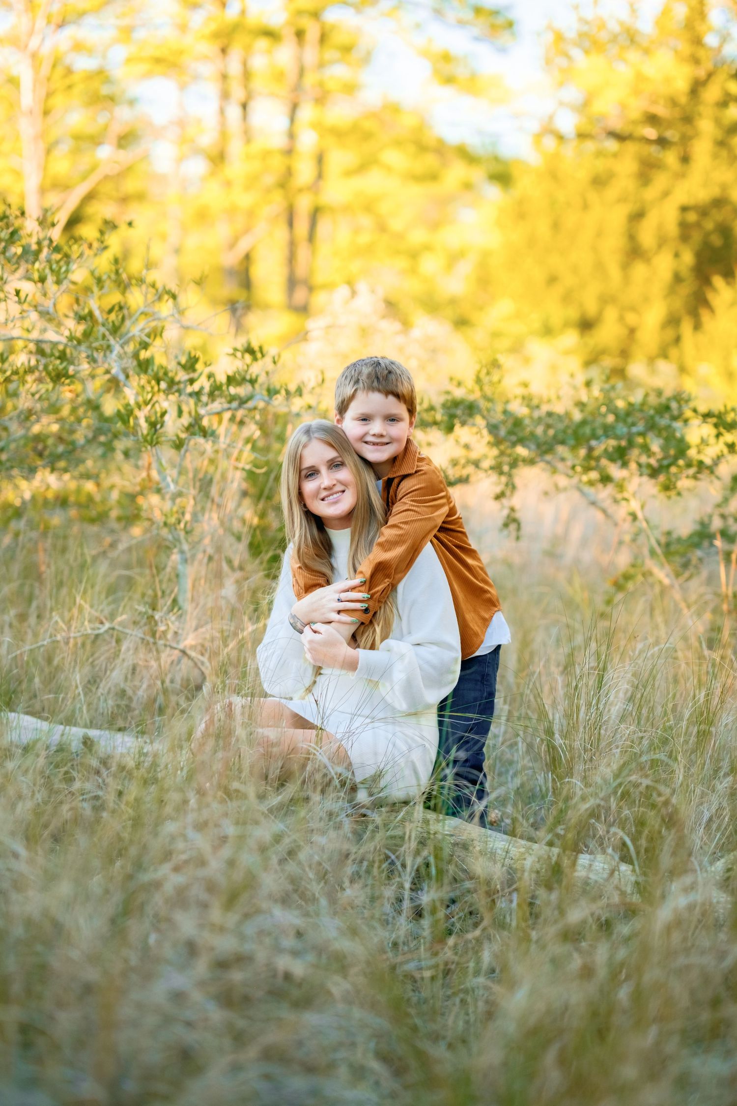 A heartwarming embrace between two people in a golden sunlit field with tall grass and trees in the background.