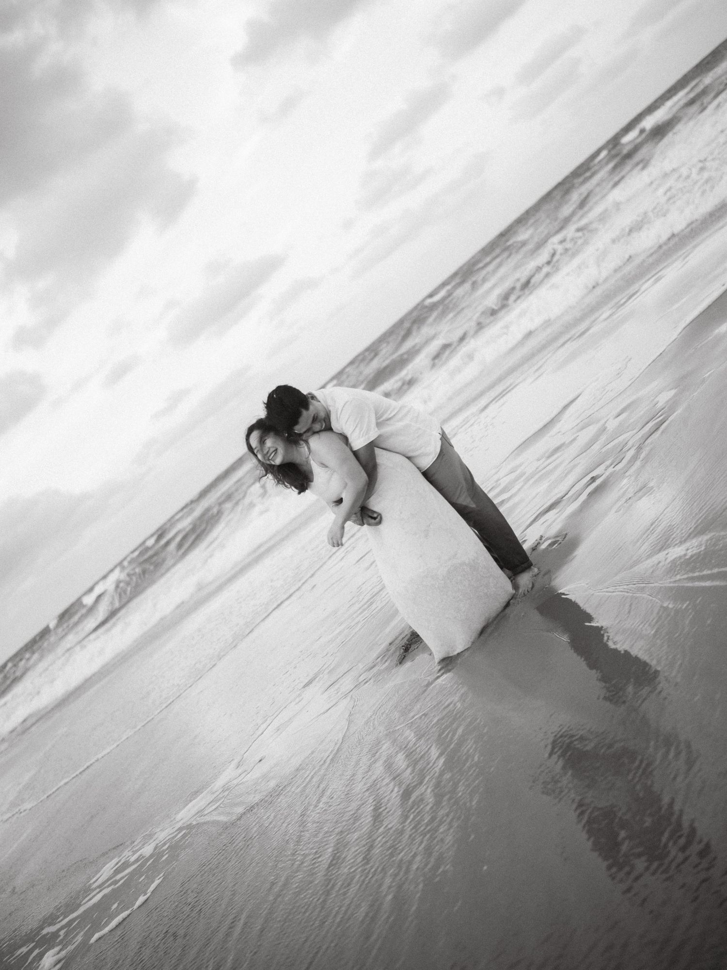 Artistic black and white photos of couple playing in ocean waves at dramatic angle.