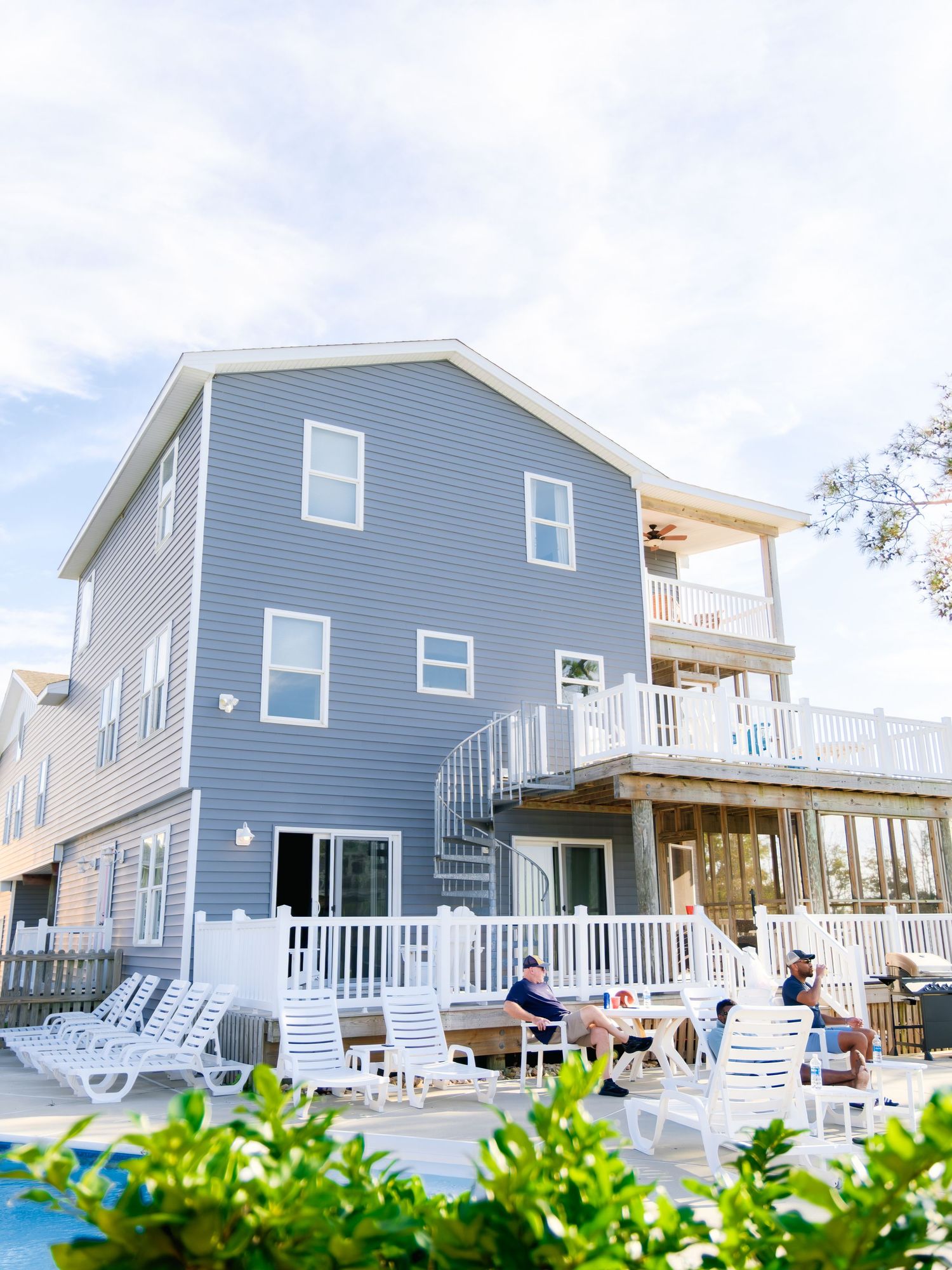 Modern blue beach houses with elevated decks and exterior stairs lined up along the oceanfront under cloudy skies.