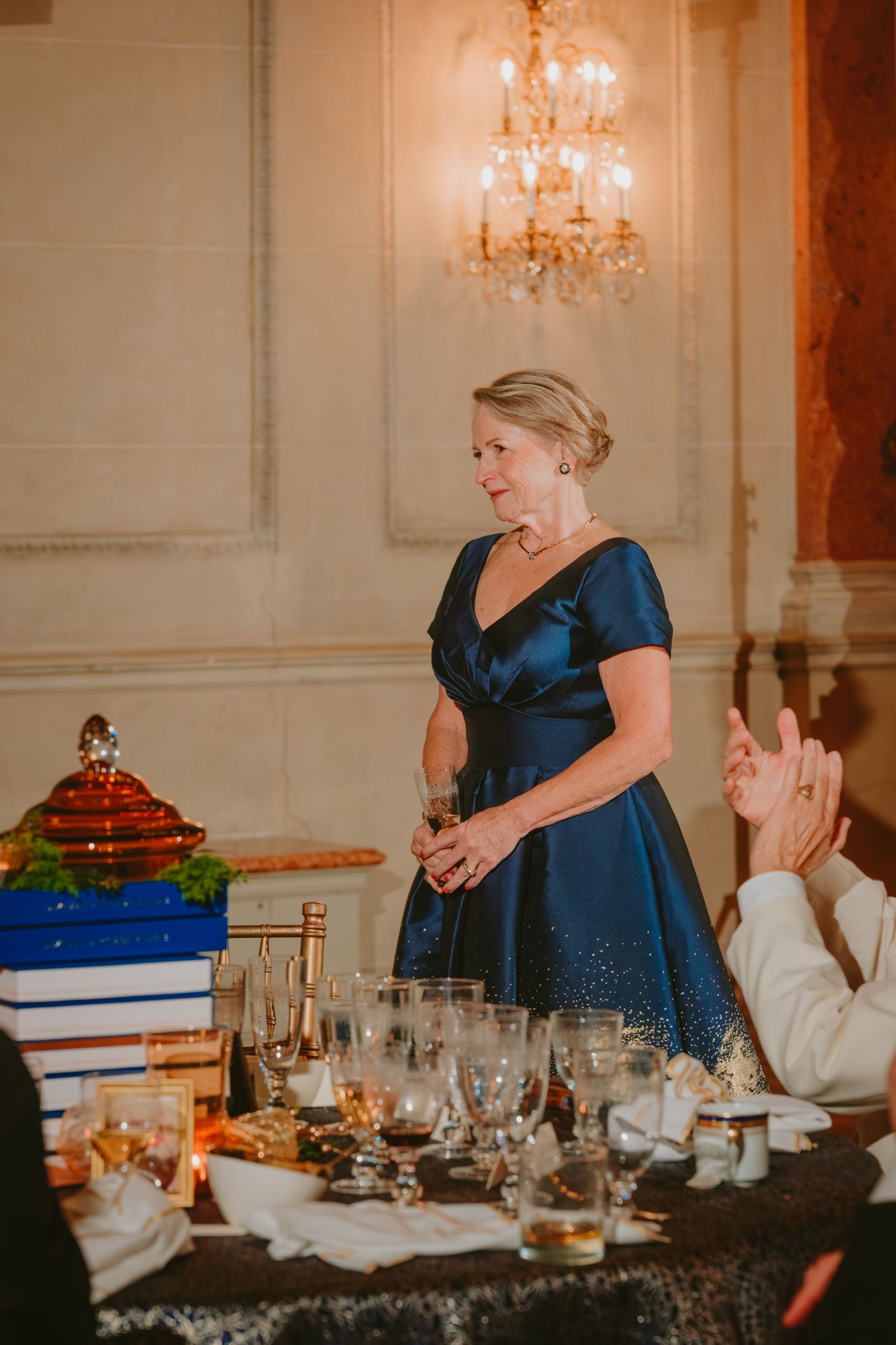 Guests seated at an elegant banquet table with crystal chandeliers and formal place settings in a luxurious dining room.