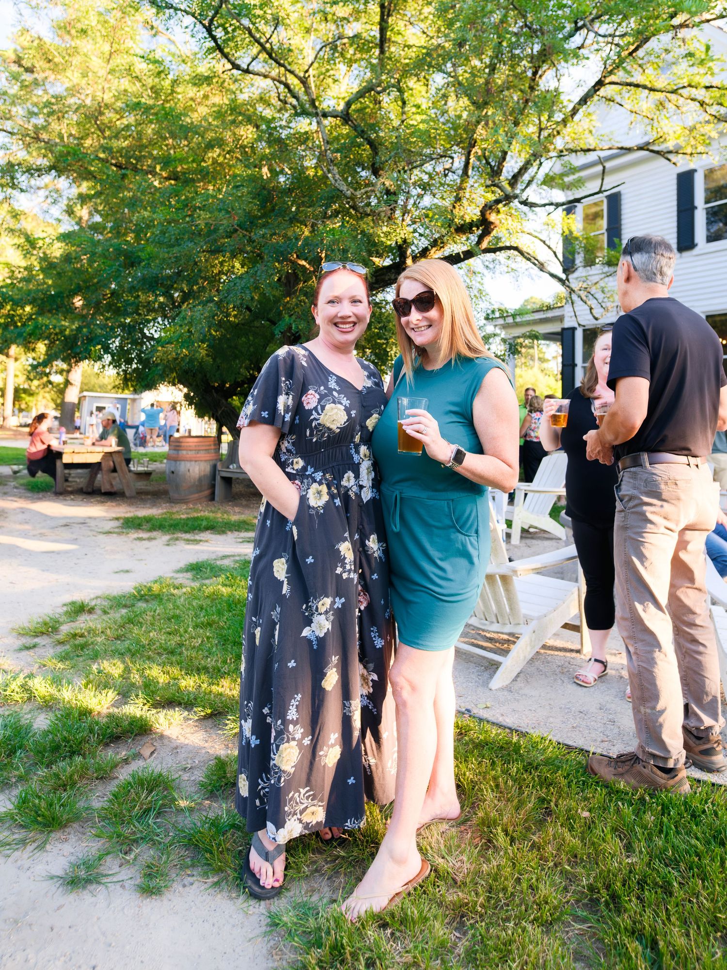 People socializing at an outdoor garden party with trees and golden sunlight in the background.