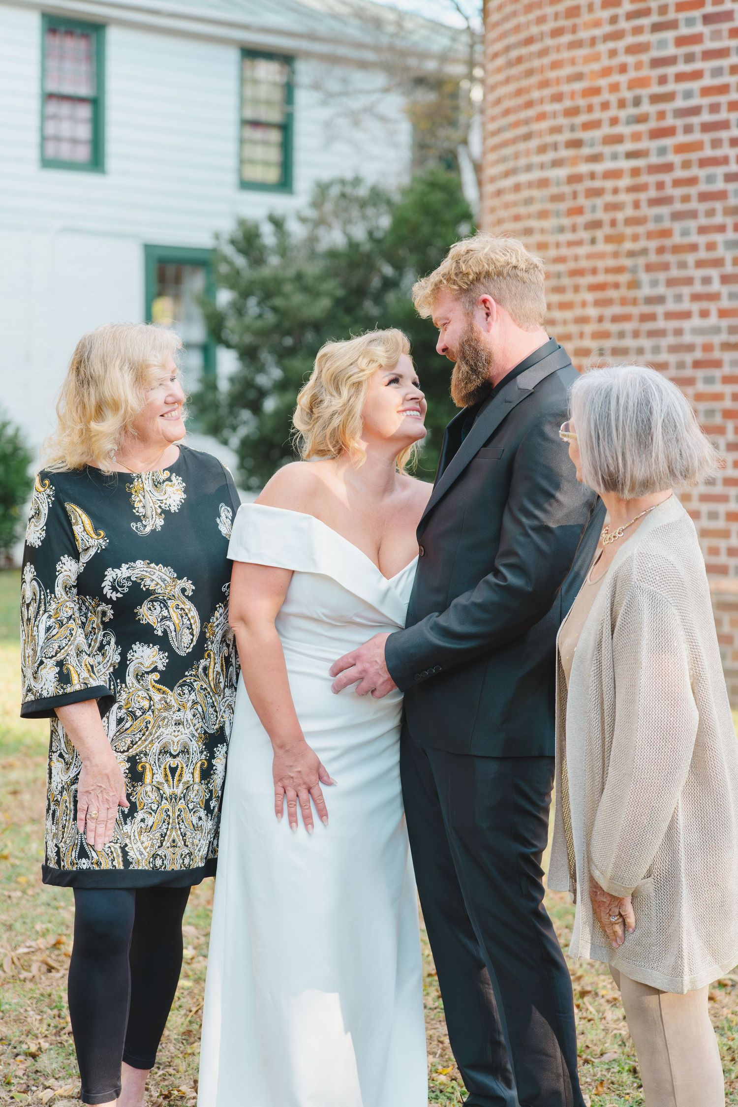 Group gathered at outdoor wedding celebration with bride in elegant off-shoulder white dress and groom in dark suit.