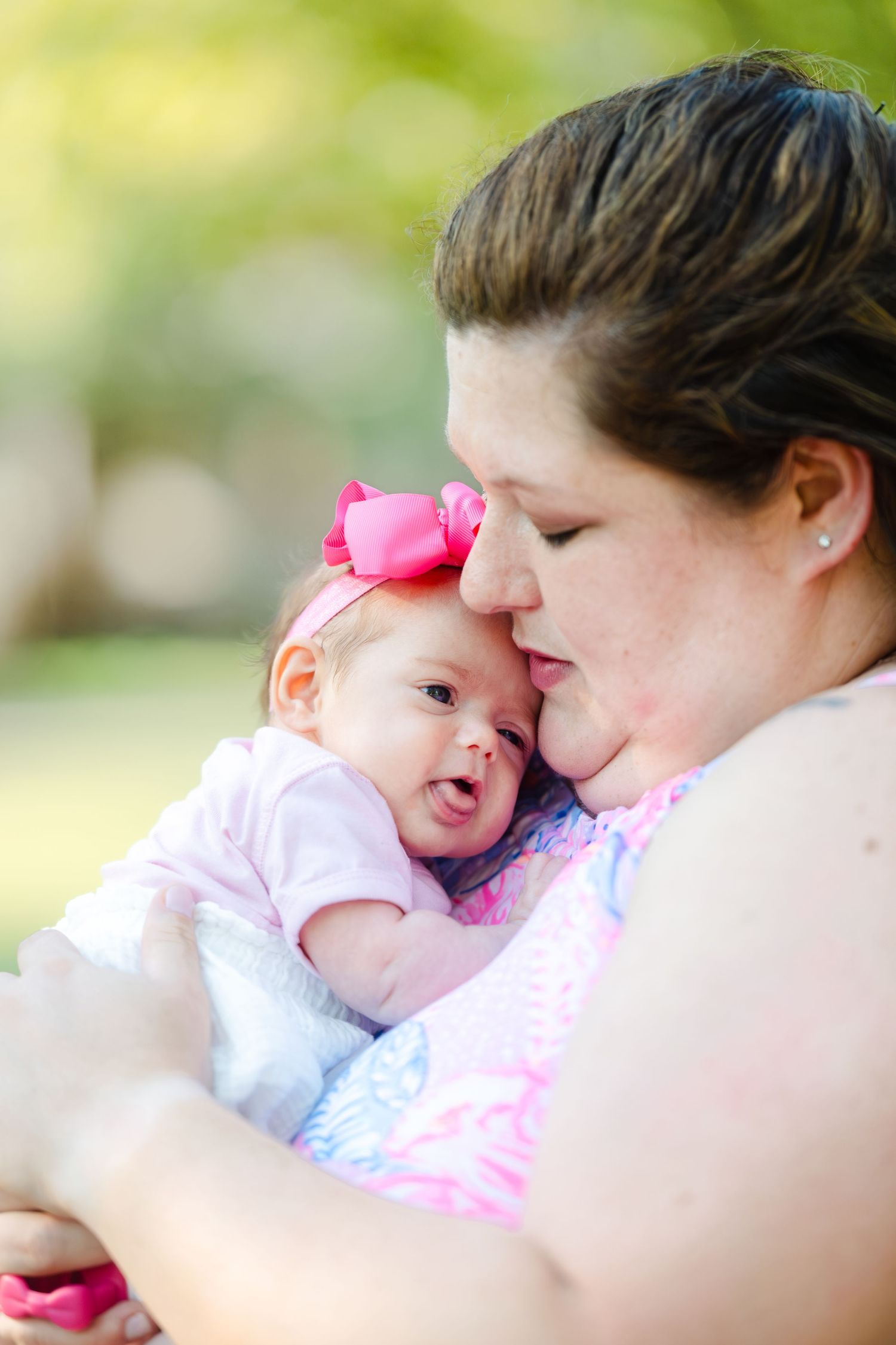 A tender moment captured between a parent and baby wearing a pink bow, shown in a soft-focus photography style.