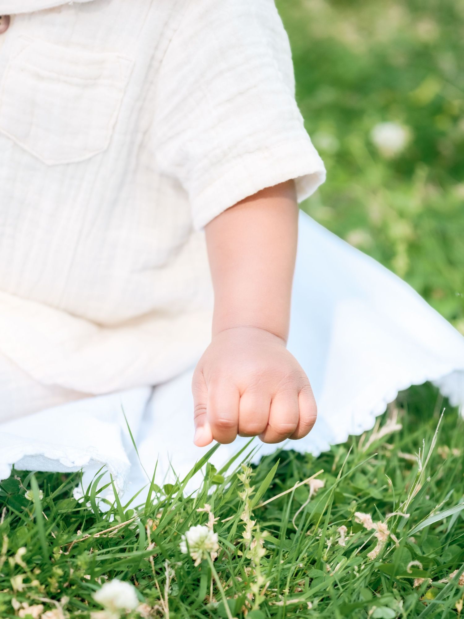 Baby feet in white clothing walking on green grass with tiny white flowers in spring or summer.