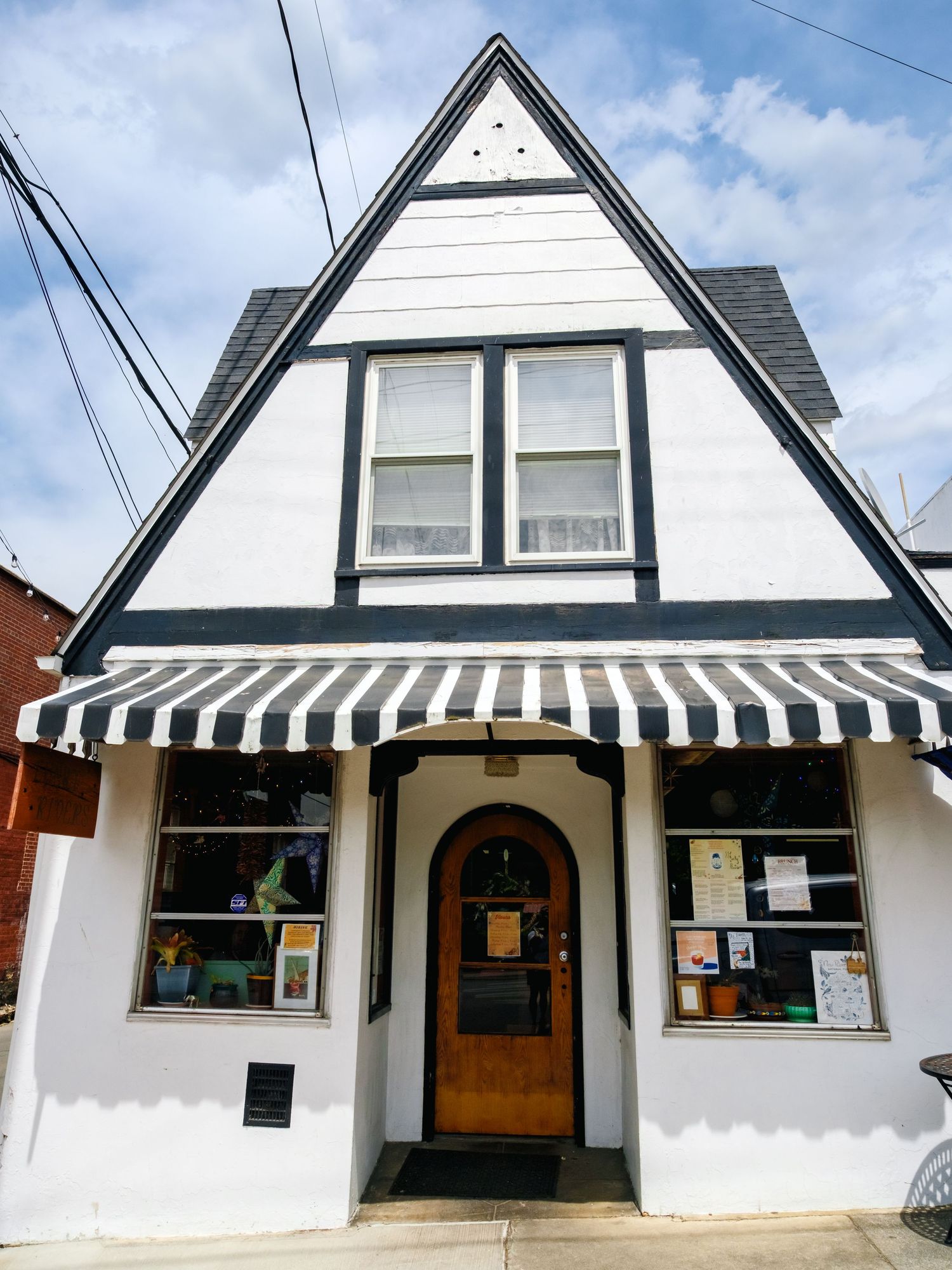 Charming white cottage-style storefront with A-frame roof, striped awning, and display windows under a blue sky.