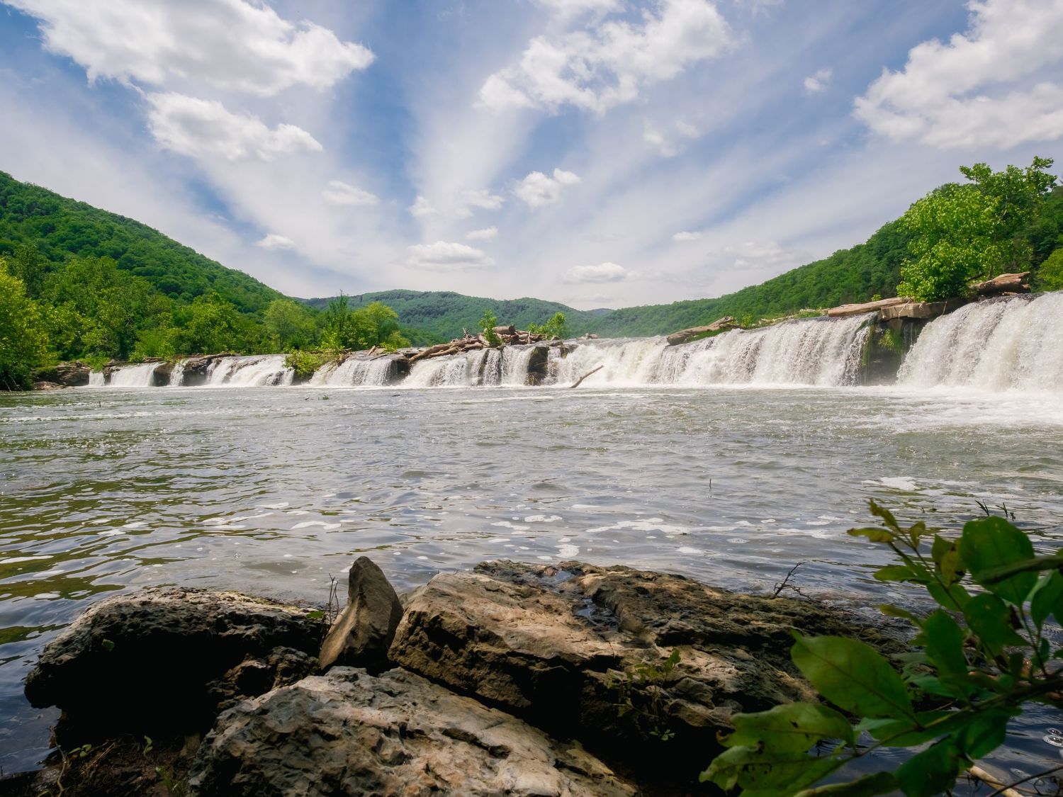 A majestic panoramic view of Kanawha Falls in West Virginia showing cascading waterfalls and lush greenery along the riverbank.