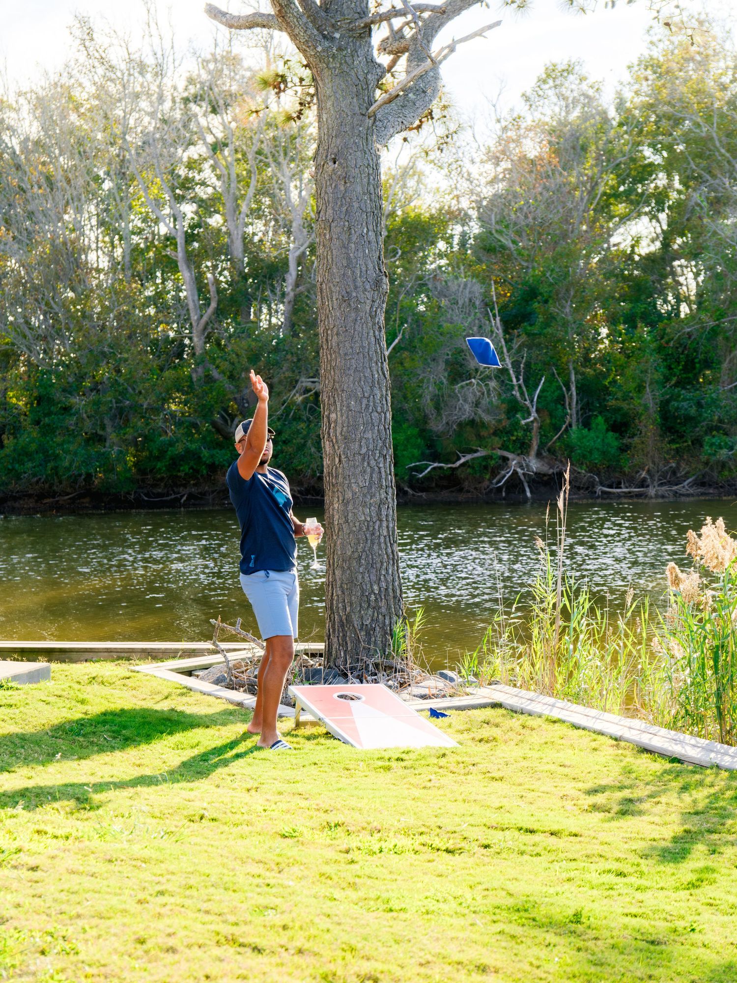 Individual practicing their golf swing form on grassy lawn beside a scenic pond on a sunny autumn day.