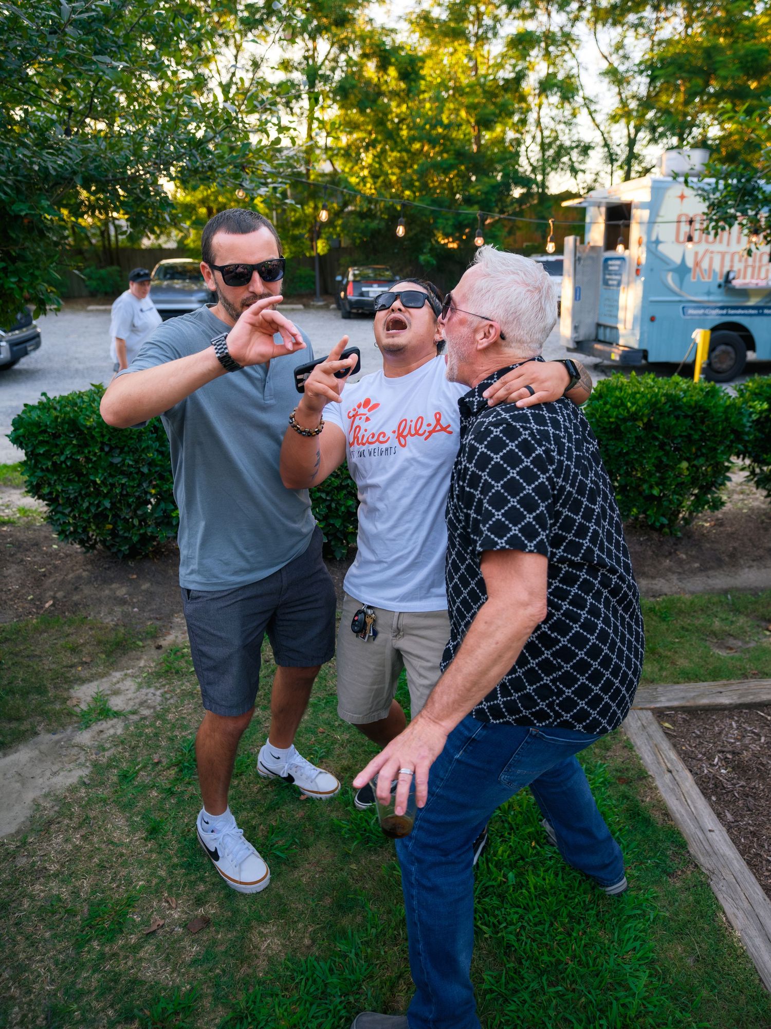A playful group poses together in a grassy outdoor setting with someone pretending to throw an exaggerated punch.