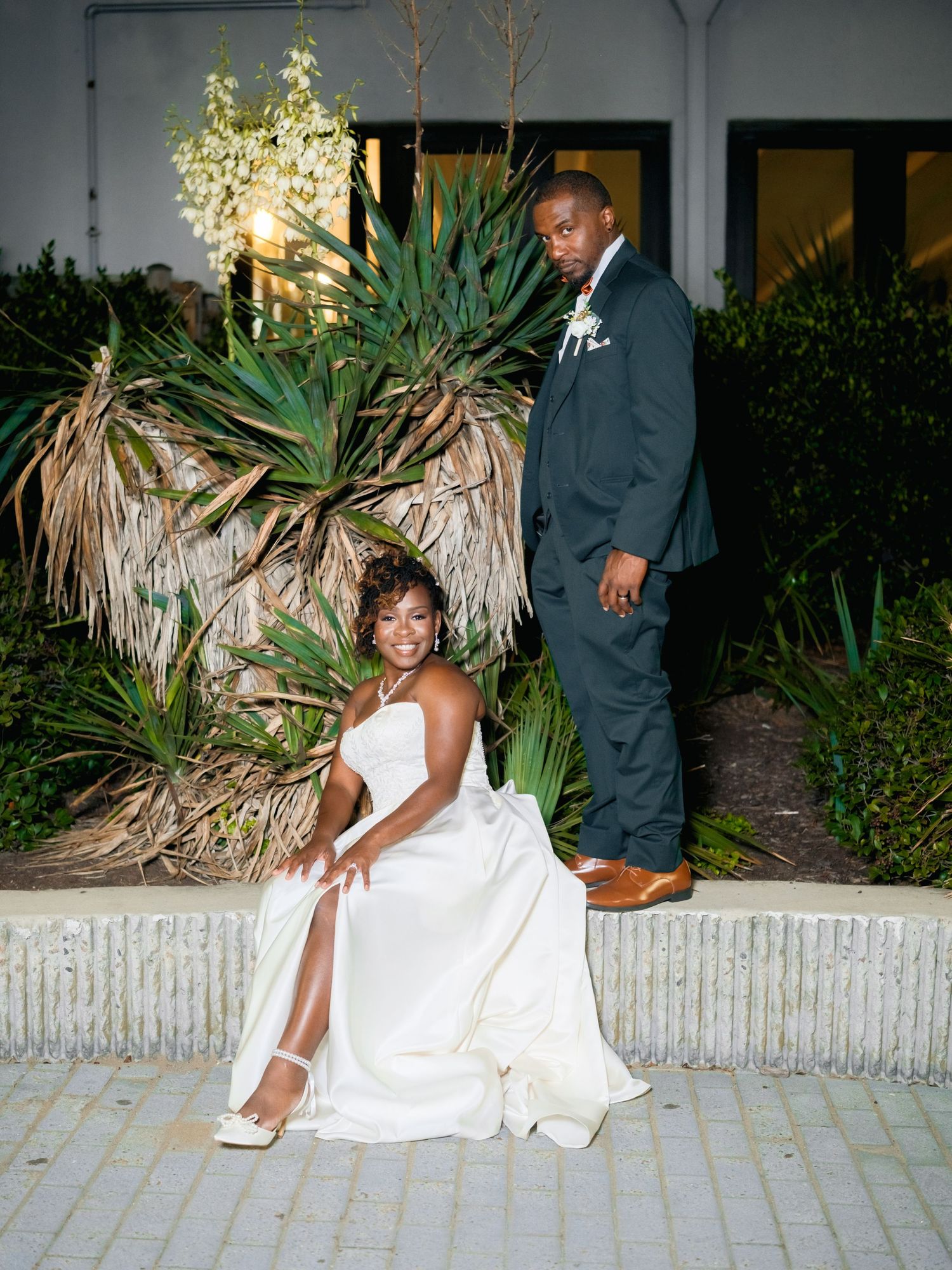 A romantic wedding photo series showing a couple posing against a tropical garden backdrop at dusk.